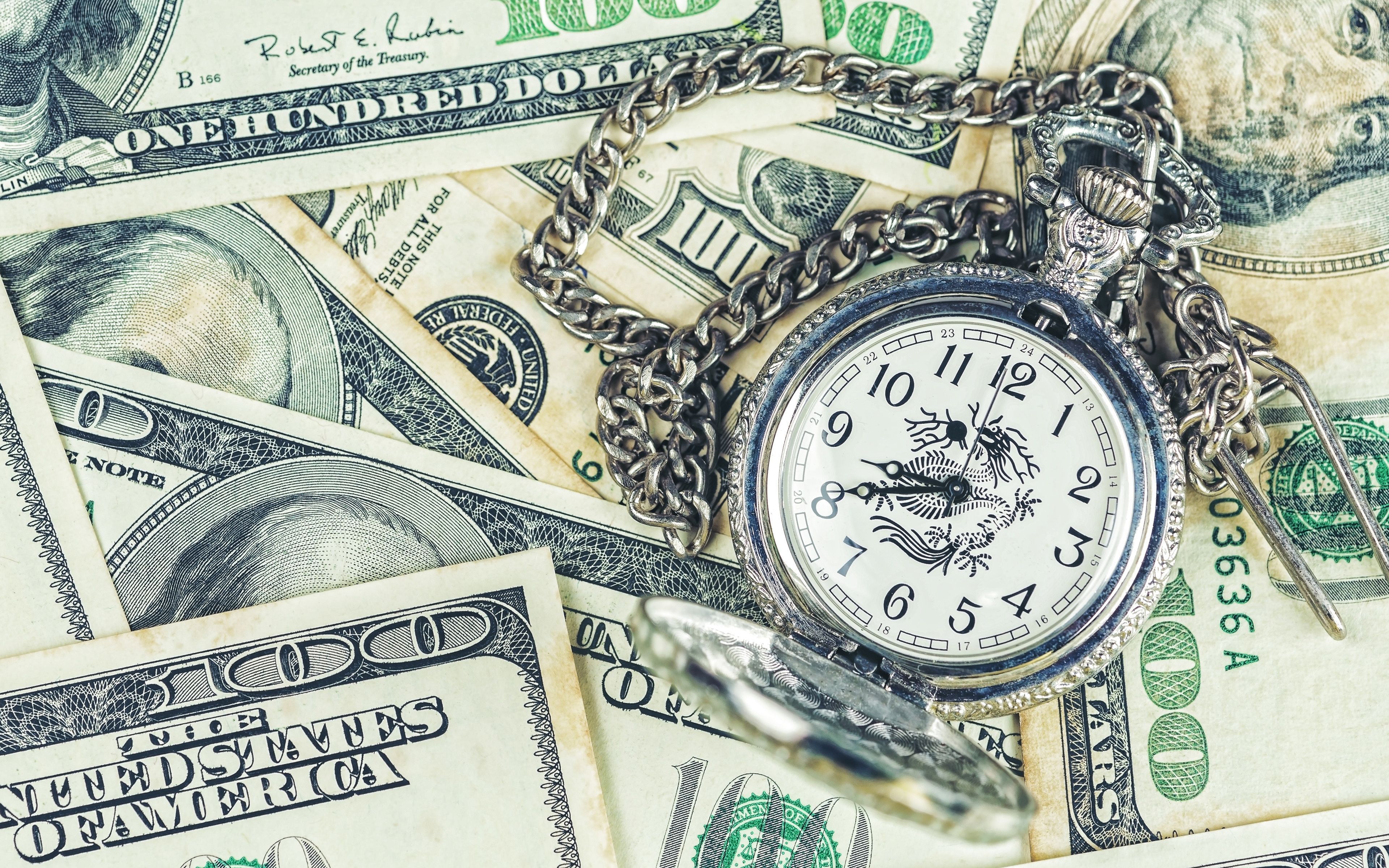 An antique pocket watch with a dragon on it, resting on a pile of US currency. - Money