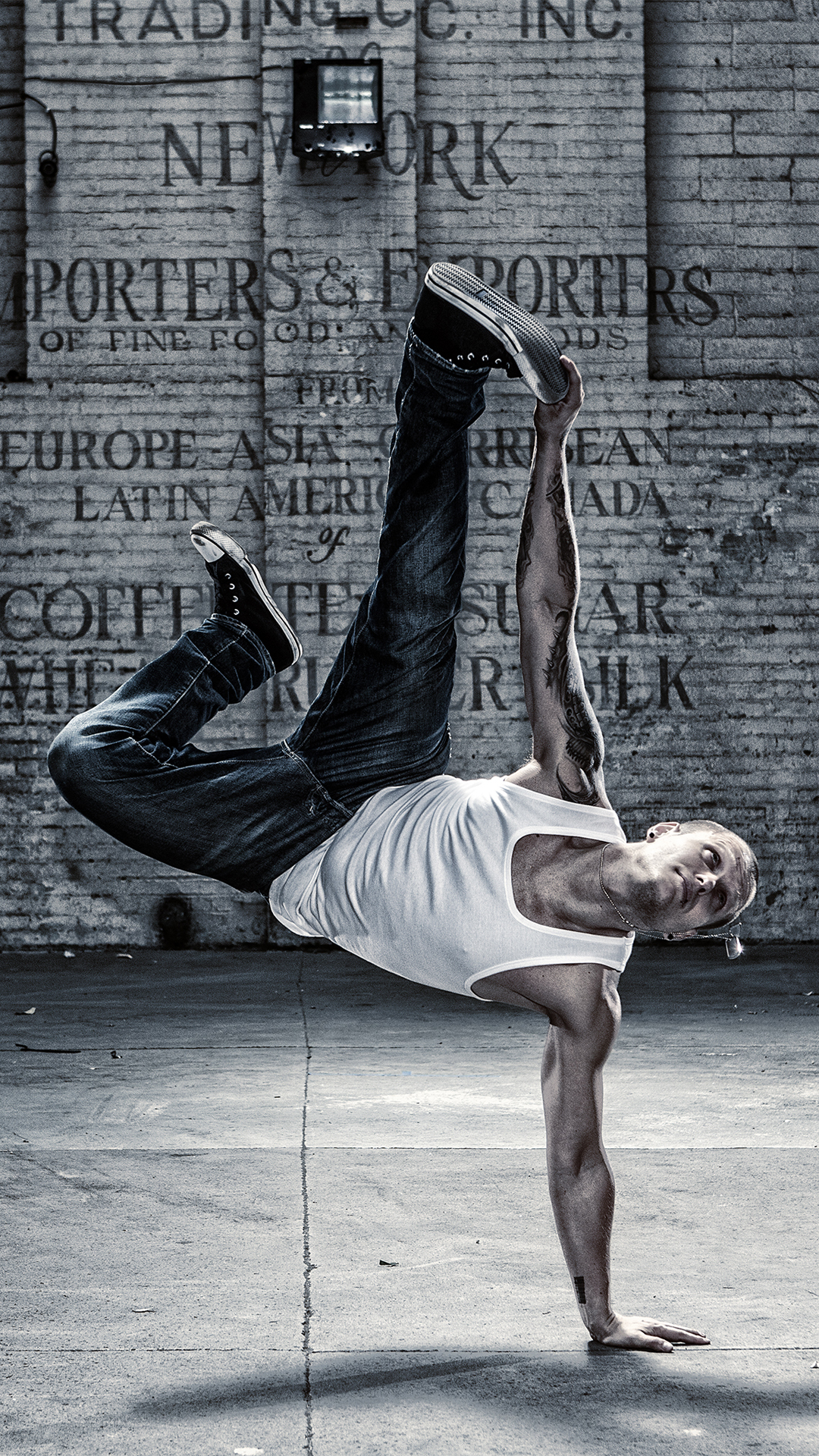 A man doing a one-handed handstand in front of a brick wall. - Dance