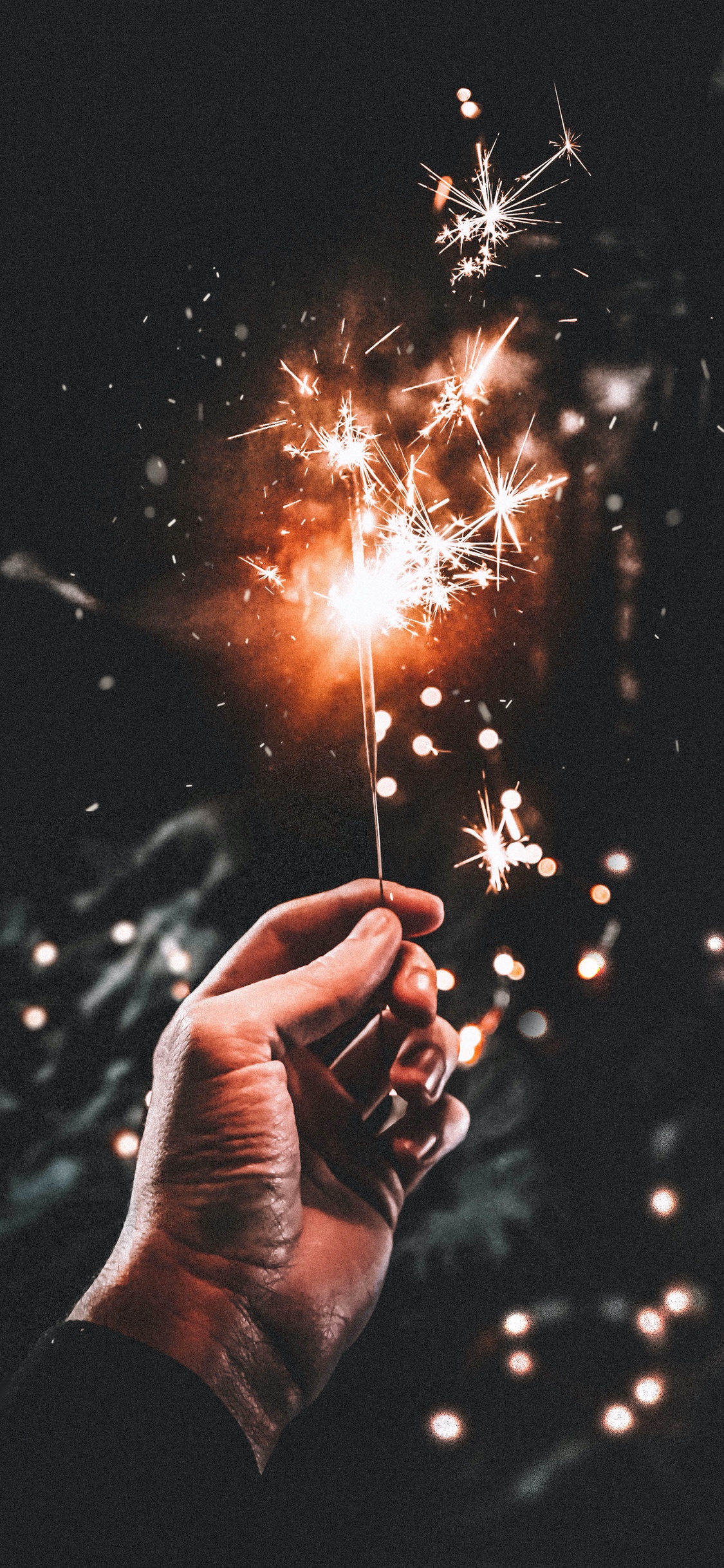 A hand holding a sparkler in the dark. - New Year