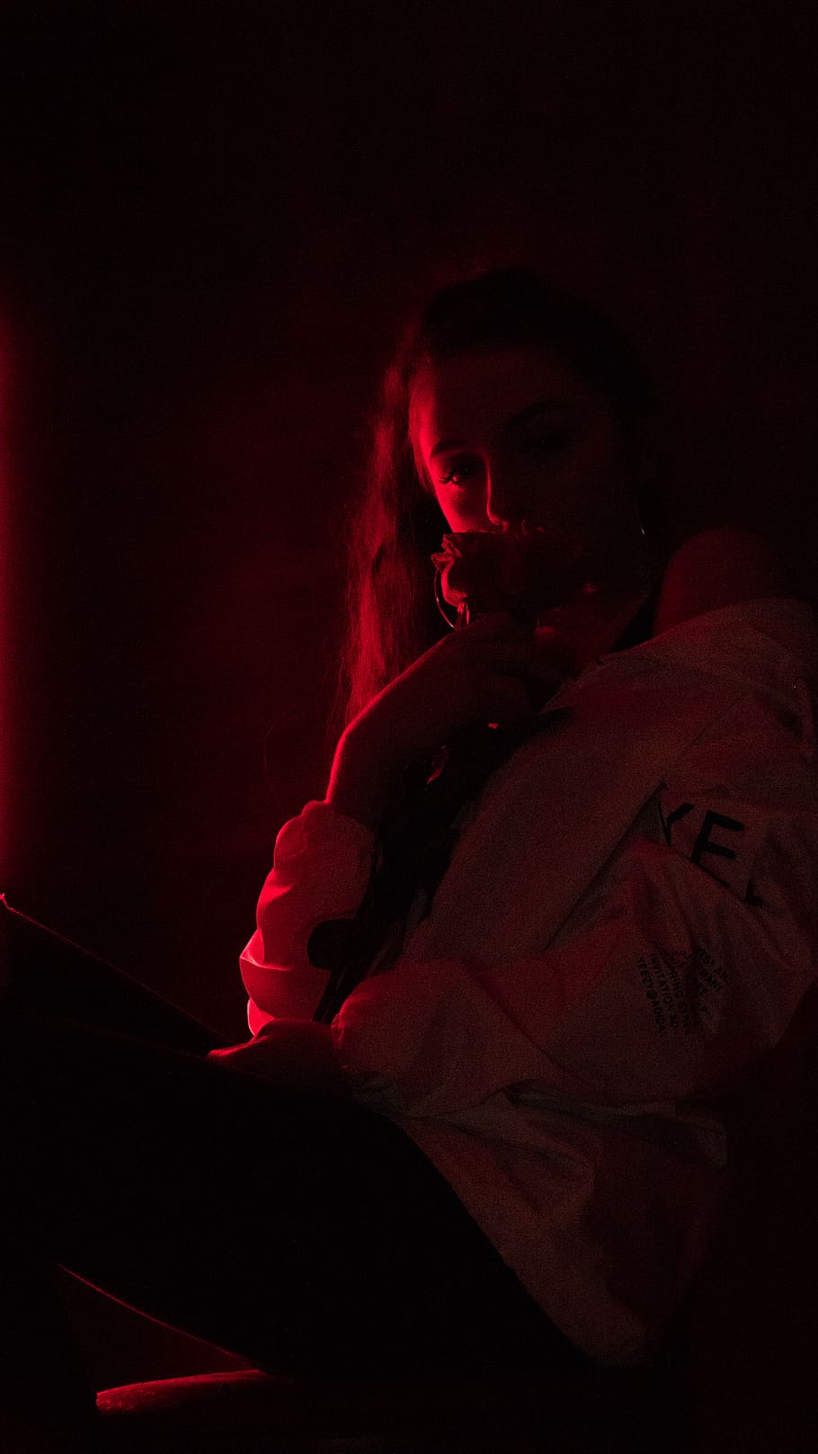 A woman in a white jacket sits in a dark room with red light - Neon red