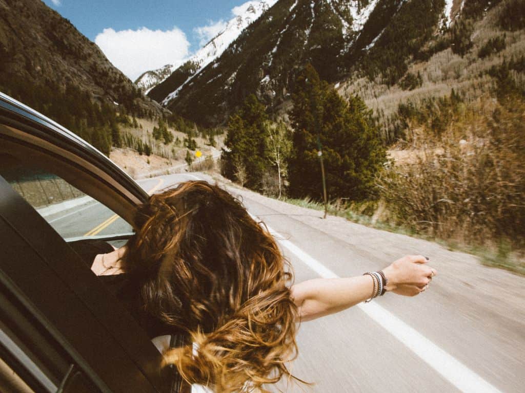 A woman with her hair blowing in the wind, leaning out of a car window - Travel