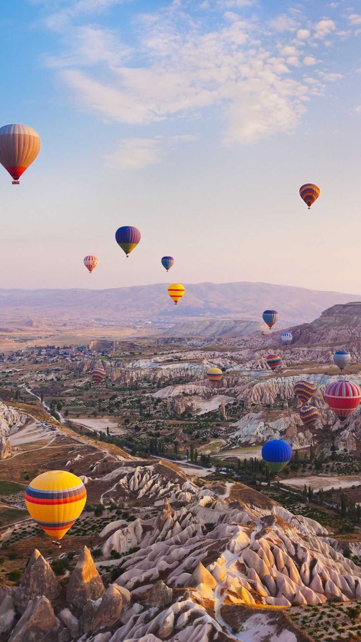 A flock of hot air balloons flying over a mountain range - Travel