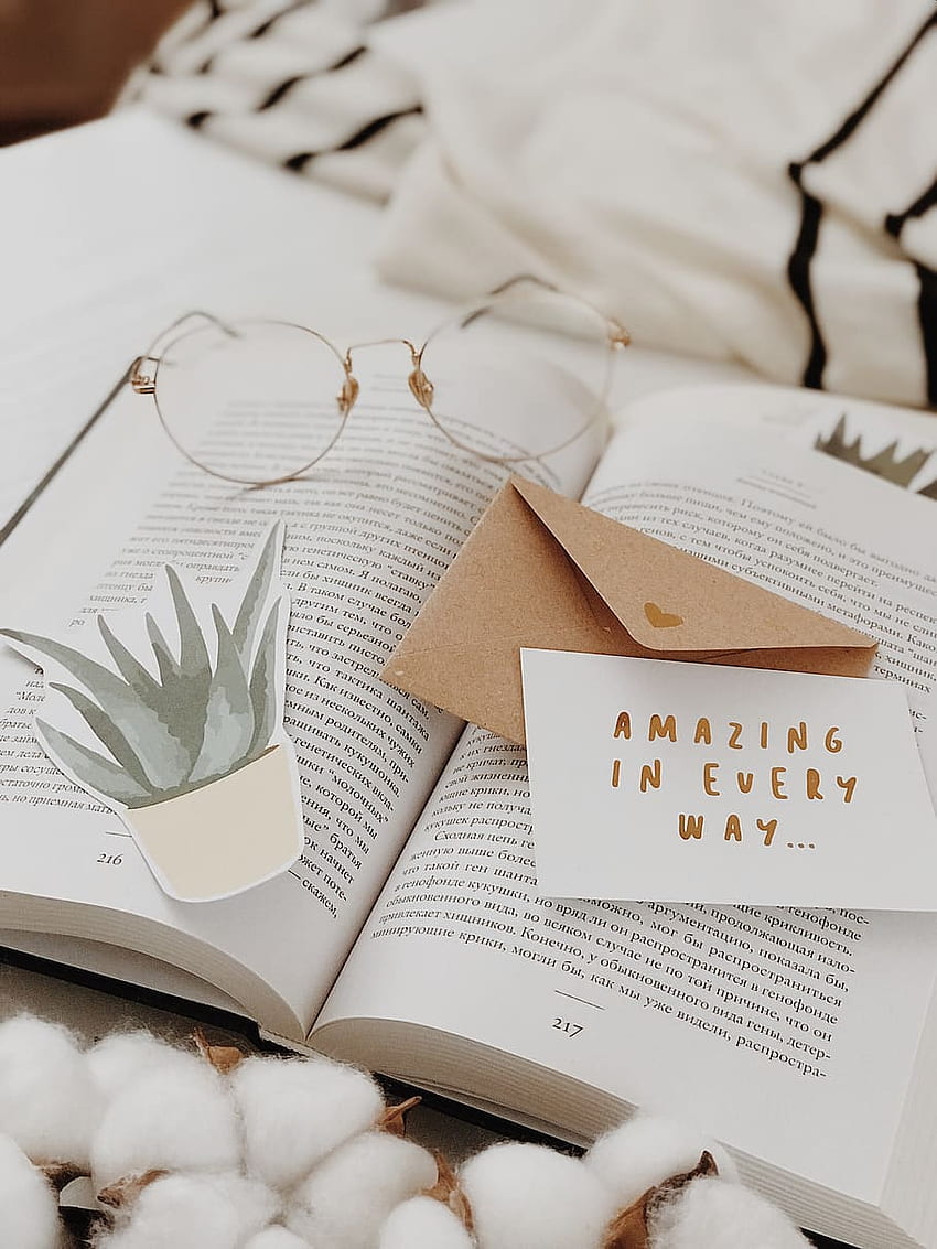 An open book with a plant shaped bookmark and a note that says amazing in every way. - Cozy, books