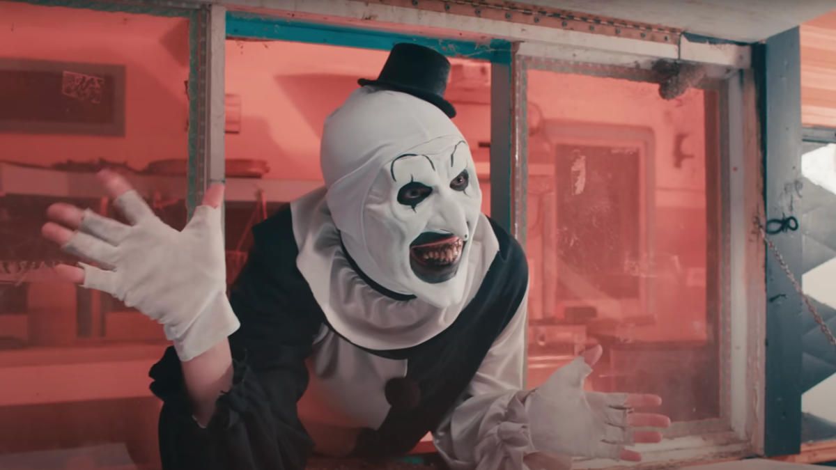 A clown in a white mask and top hat crouches in a red-lit room. - Clown