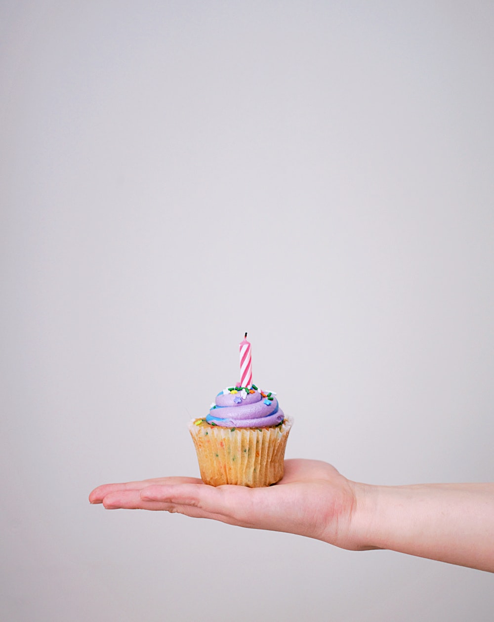 A person holding a cupcake with a candle on it. - Birthday, bakery, cupcakes