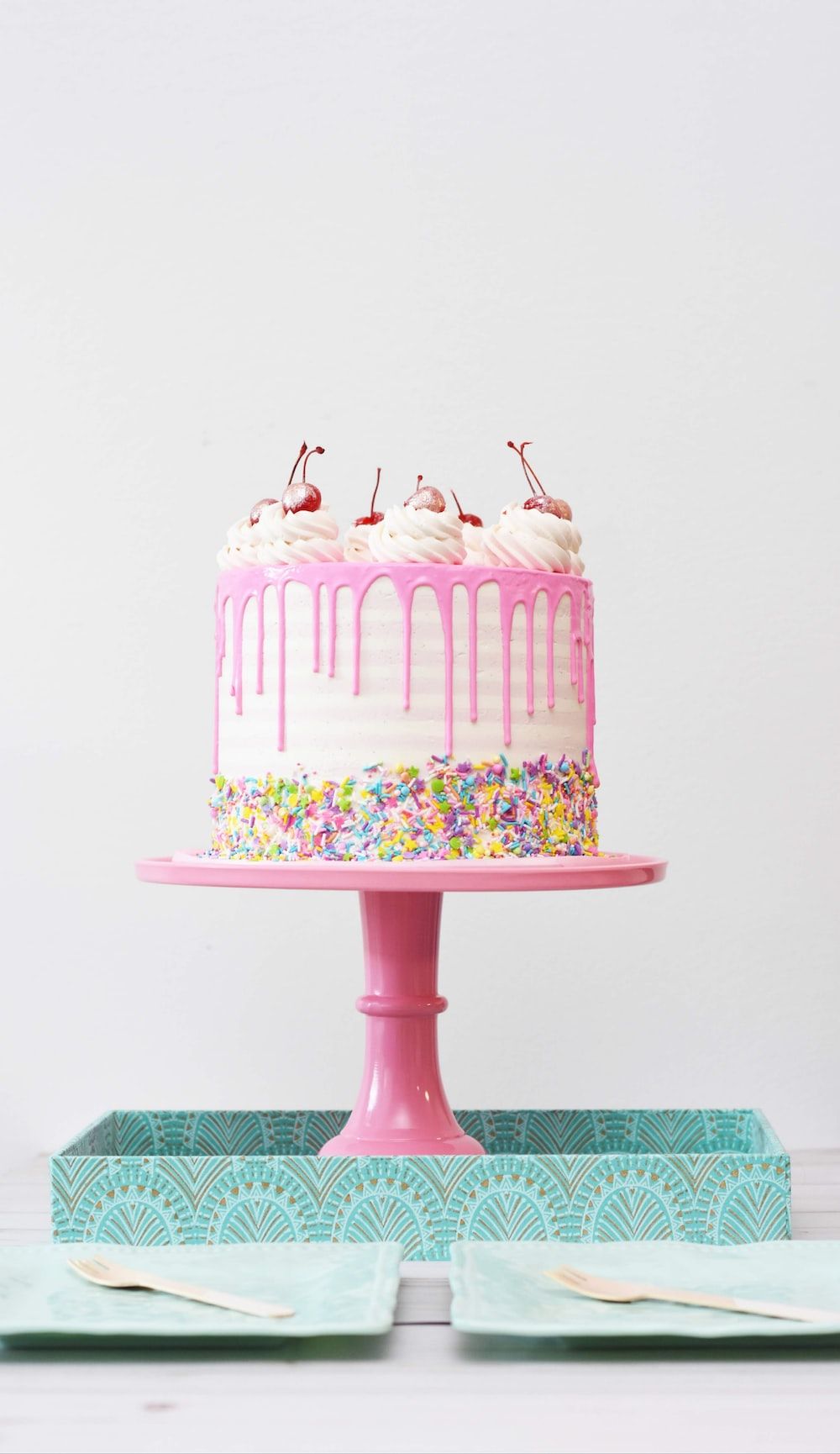 A cake with pink icing and sprinkles on a pink cake stand. - Birthday, cake