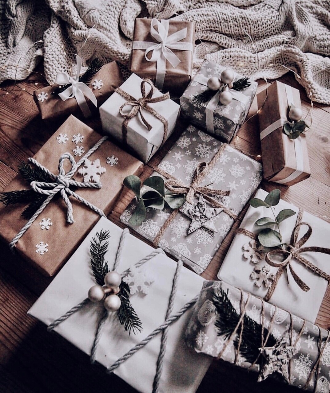 A table with many wrapped gifts with white and brown paper and string. - Silver