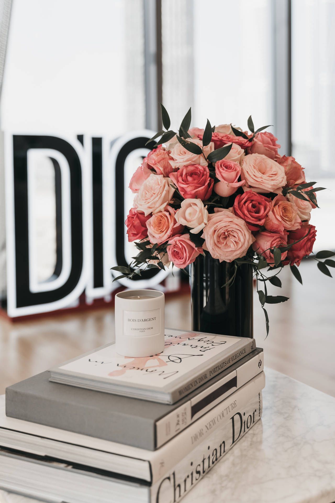 A vase of roses sits on a table with books. - Dior