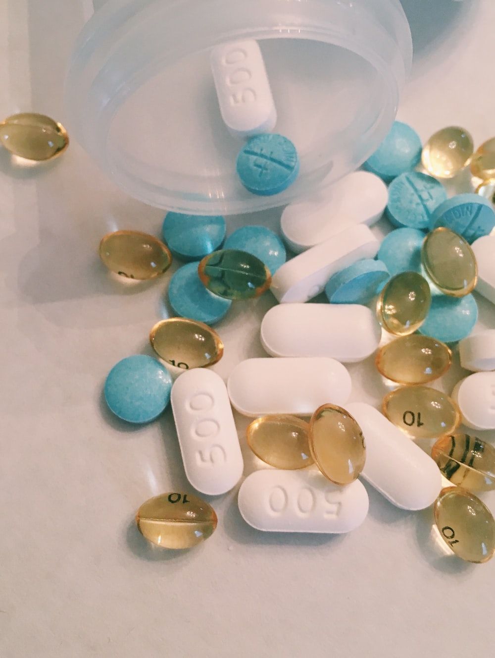 A bottle of pills, some of which are blue, white, and yellow. - Medical