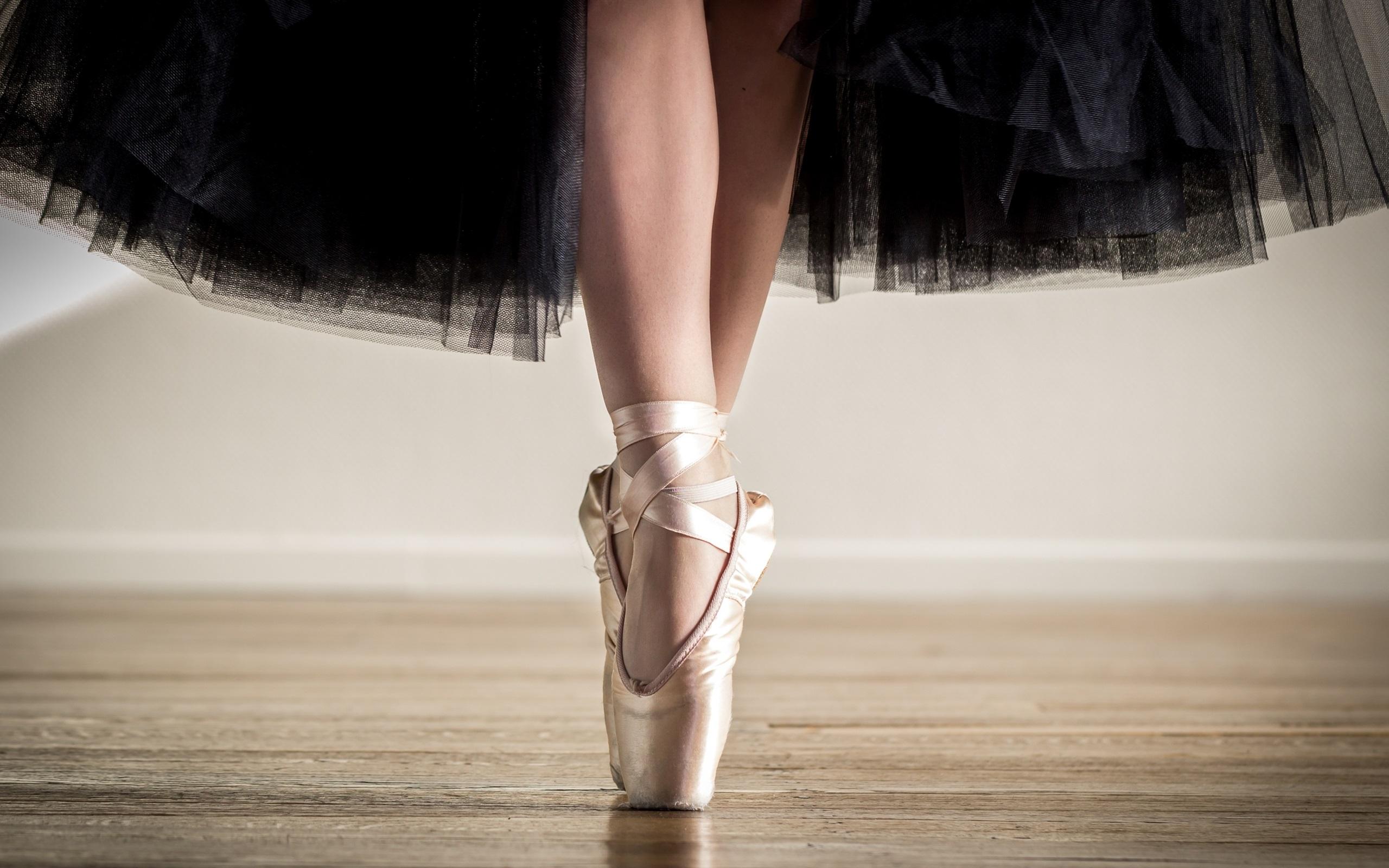 A ballerina's feet in pointe shoes, with her black tutu flowing in the background. - Ballet