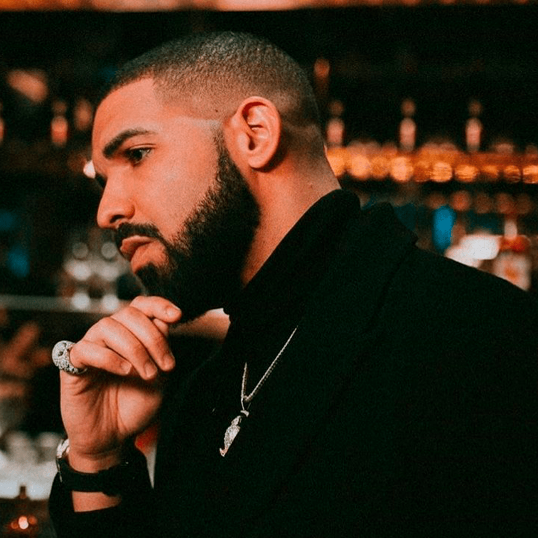 Drake is seen in a side profile wearing a black jacket and a silver chain around his neck. - Drake