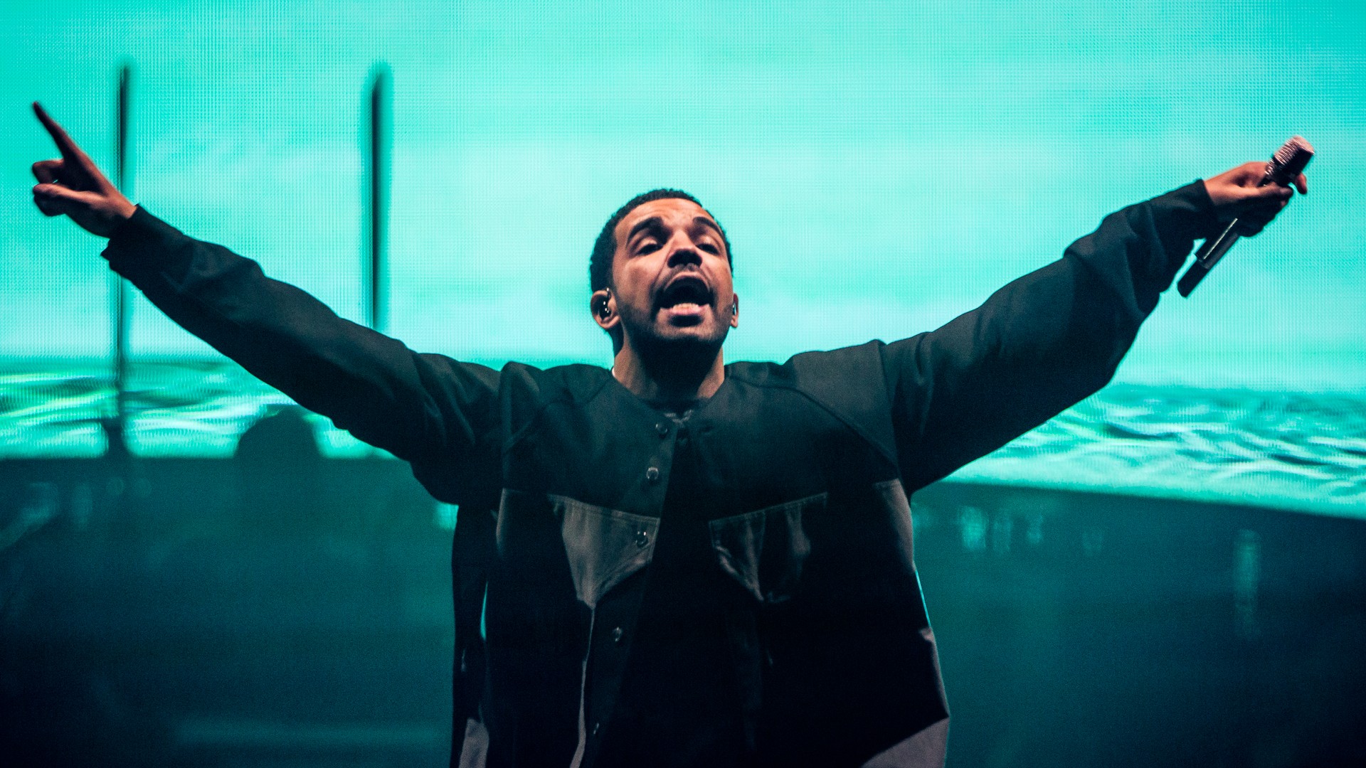 Drake holding a microphone and standing in front of a blue screen - Drake