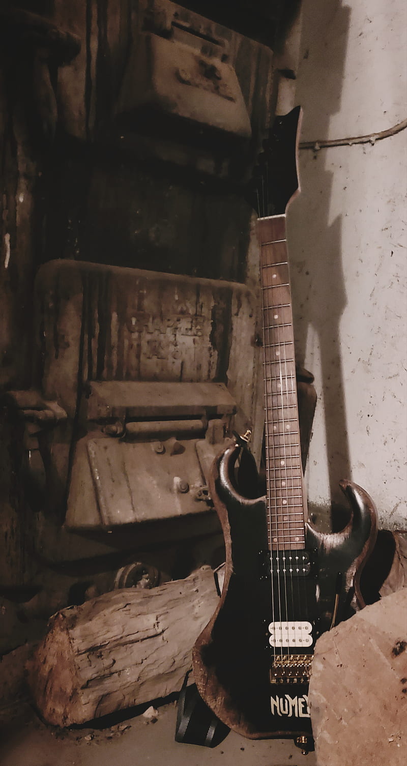 An electric guitar leaning against a pile of wood in a room. - Guitar