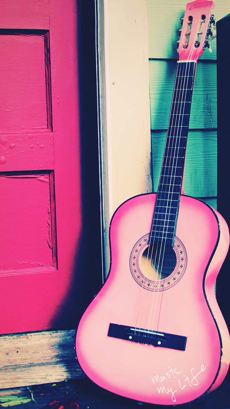 A pink guitar sits next to a red door. - Guitar