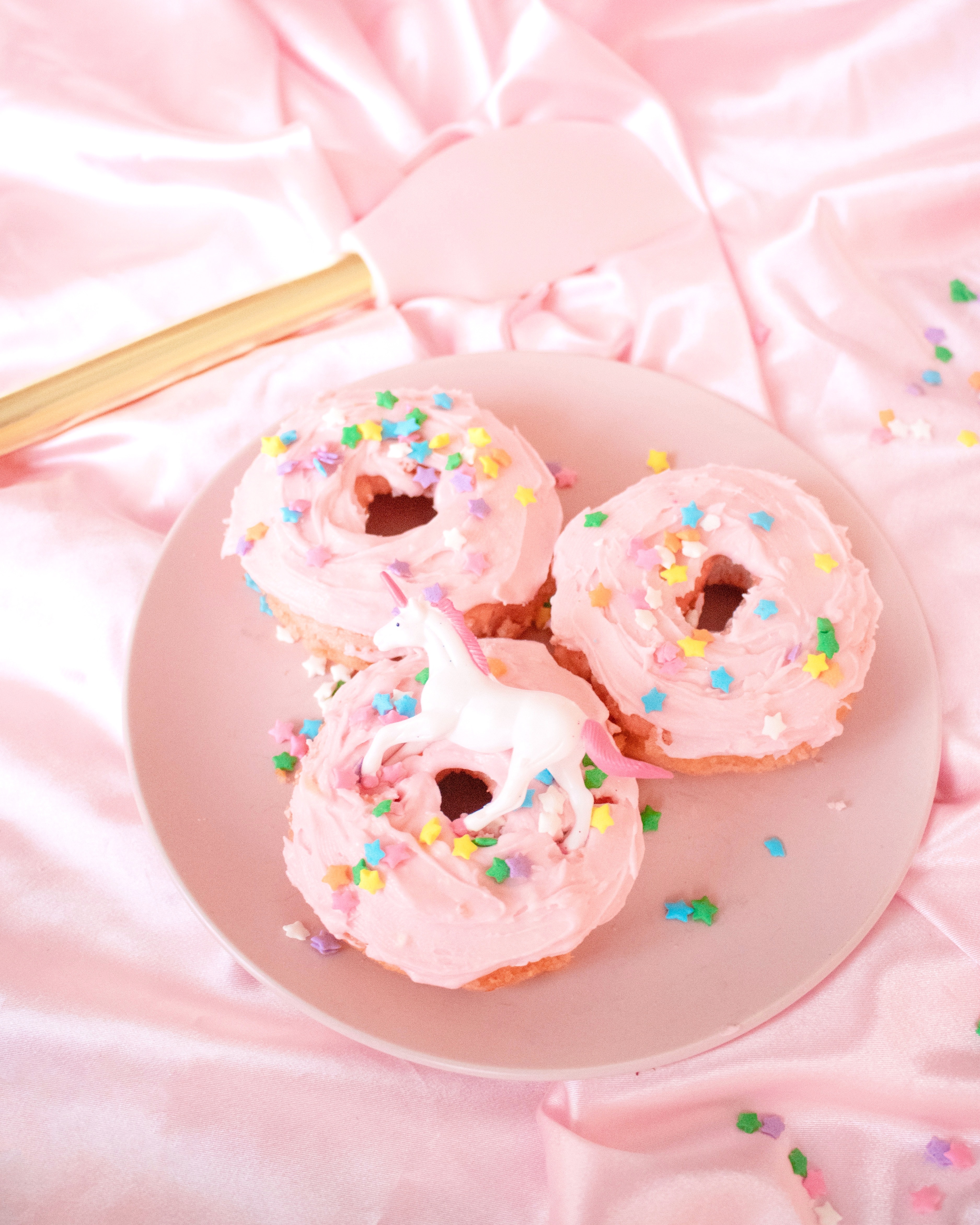 A plate of three pink donuts with sprinkees on top - Bakery