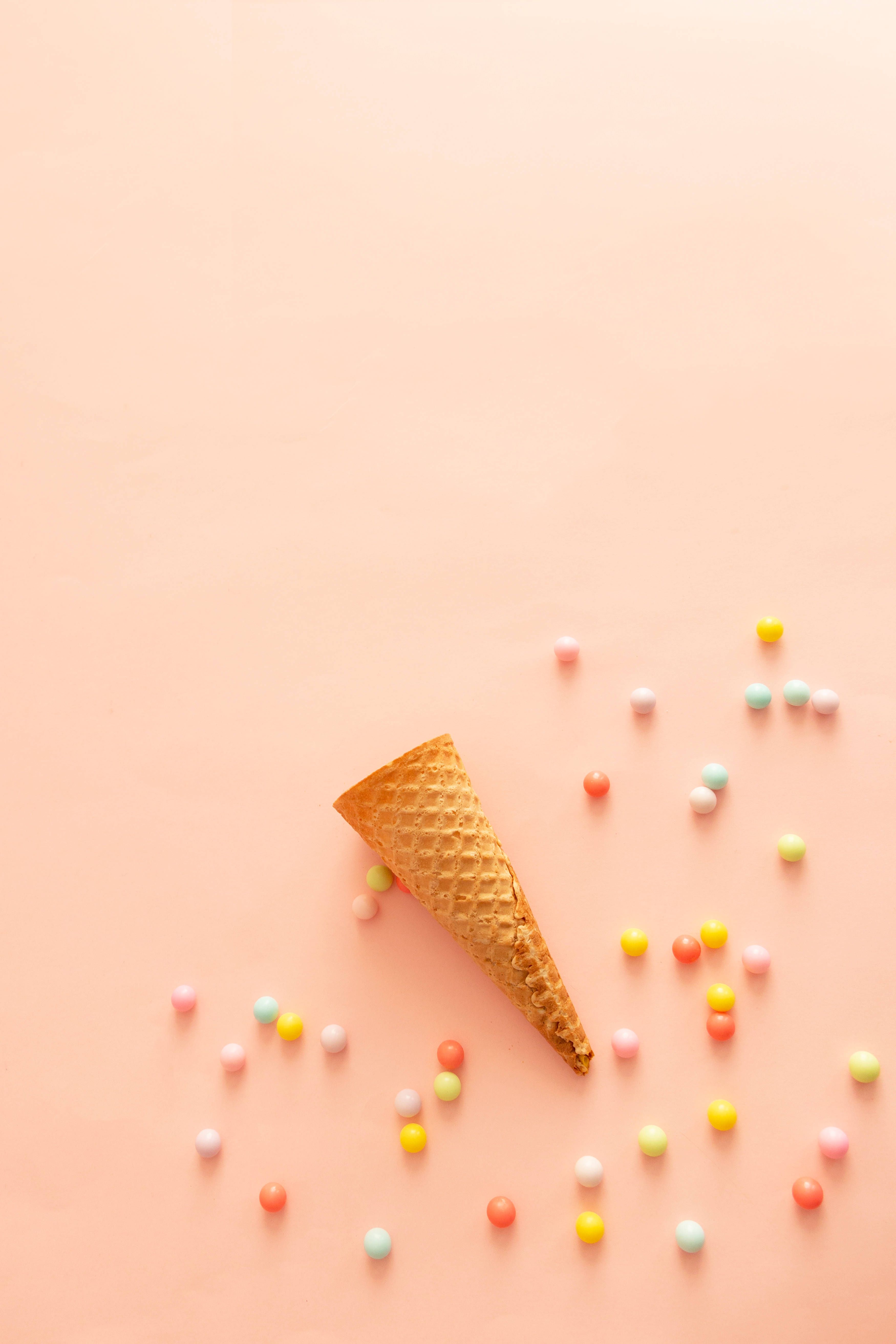 A waffle cone on a pink background with scattered candy. - Foodie