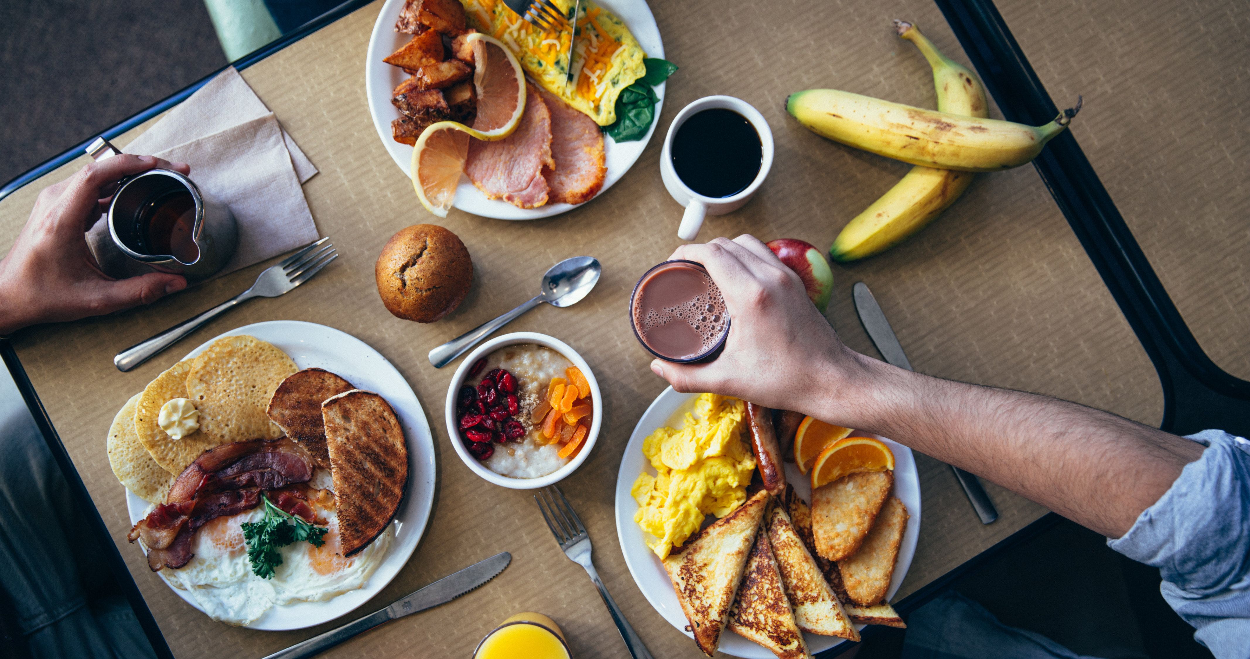 Two people enjoying a breakfast spread with coffee, toast, eggs, and fruit. - Foodie, food