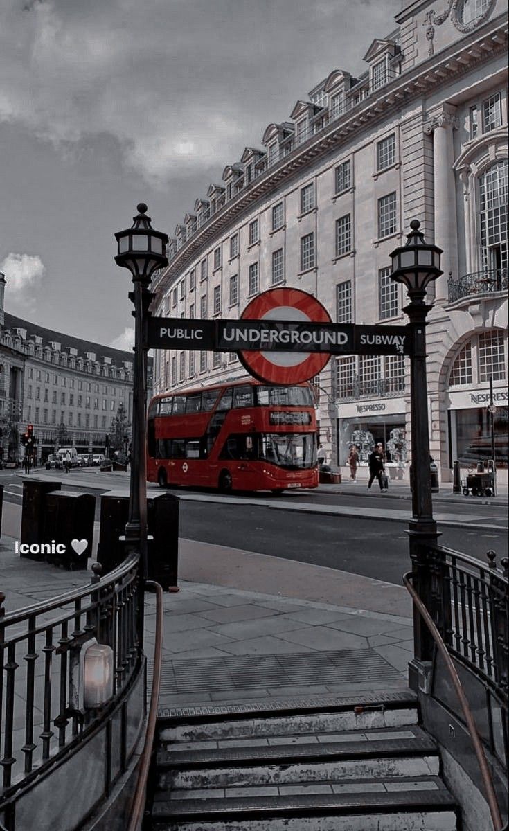 Red double decker bus passing under a public underground subway sign. - London