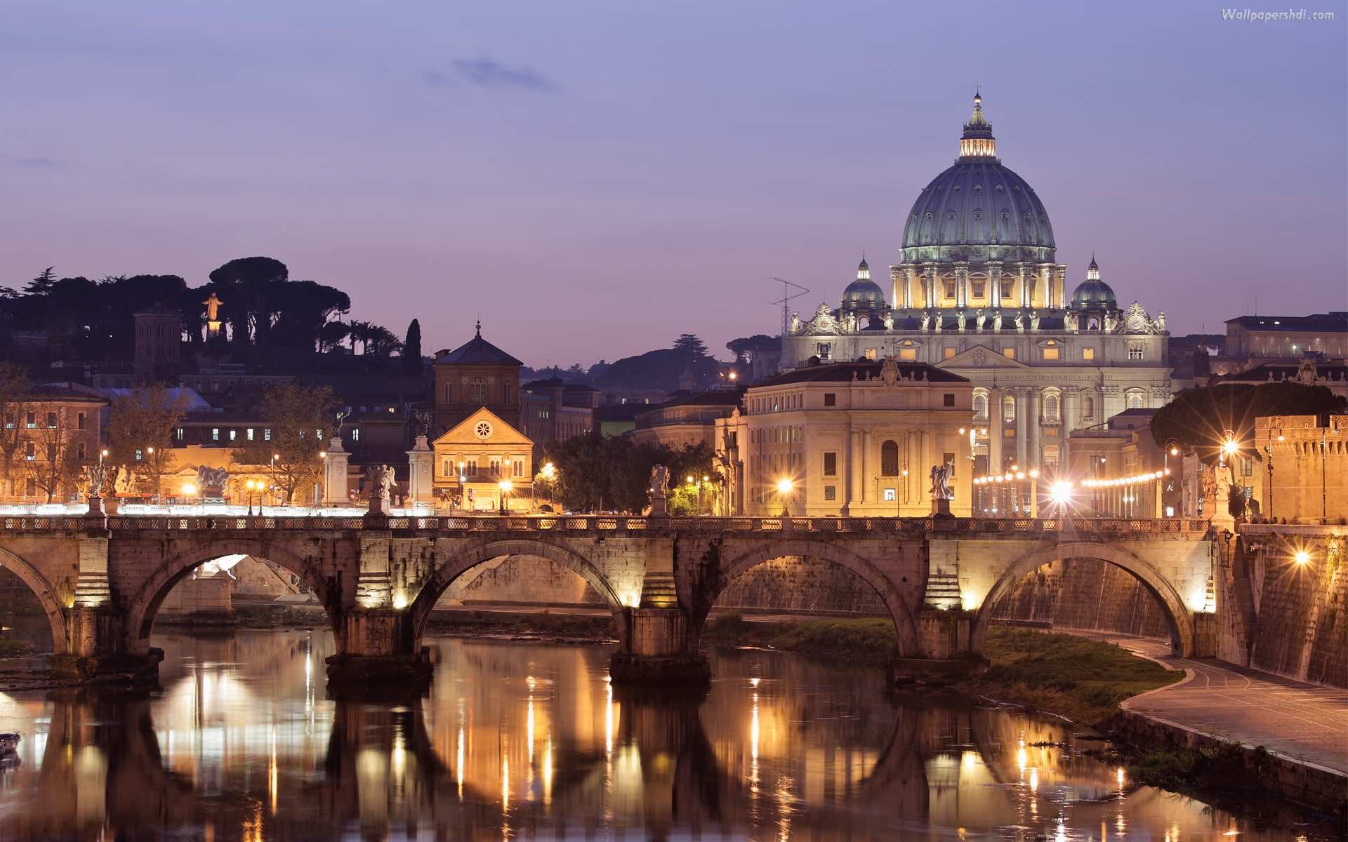 The dome of St. Peter's Basilica and the bridge over the Tiber river in Rome at night. - Italy