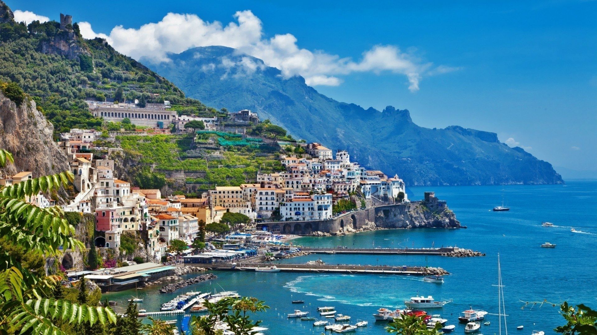 Boats are docked in the water near a mountain. - Italy