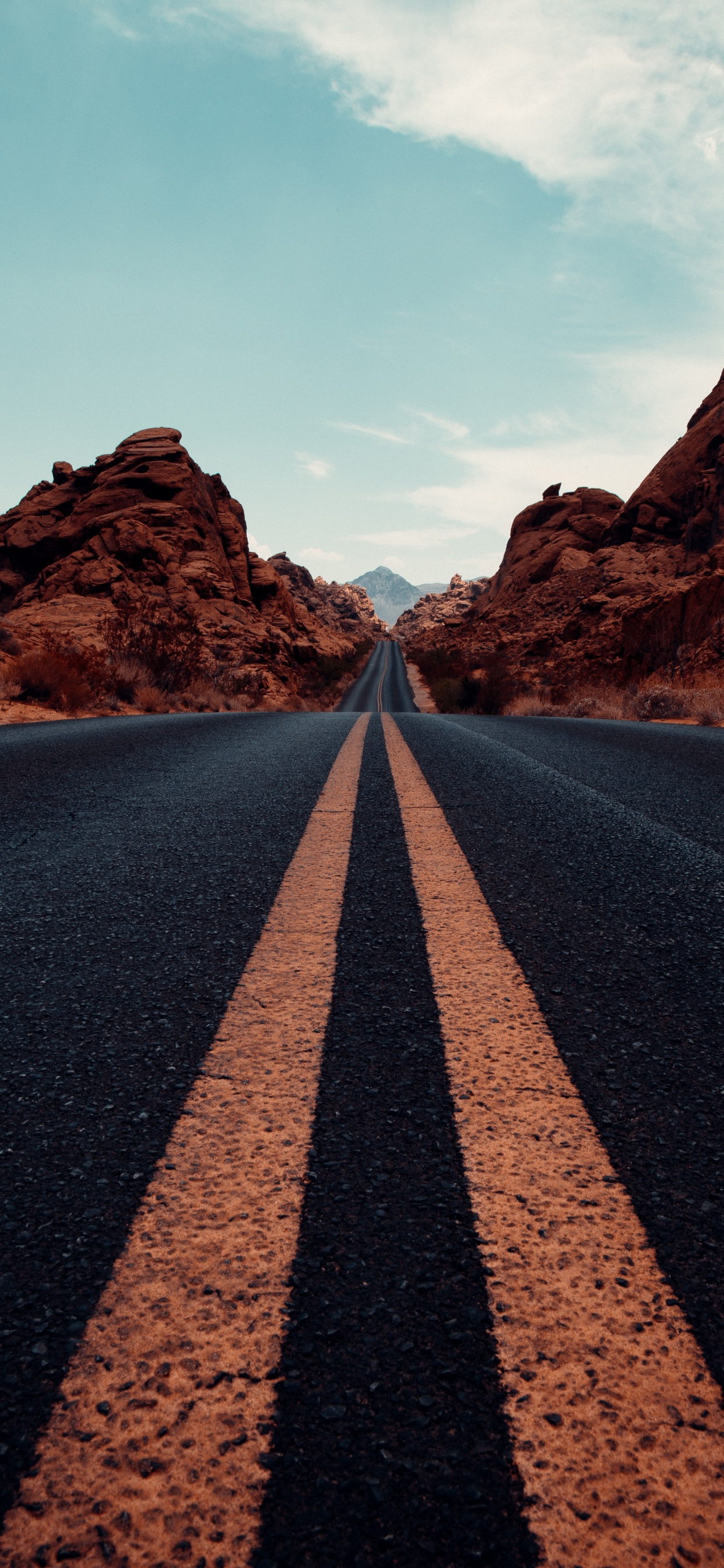 An empty road surrounded by red rocks and a blue sky. - Road