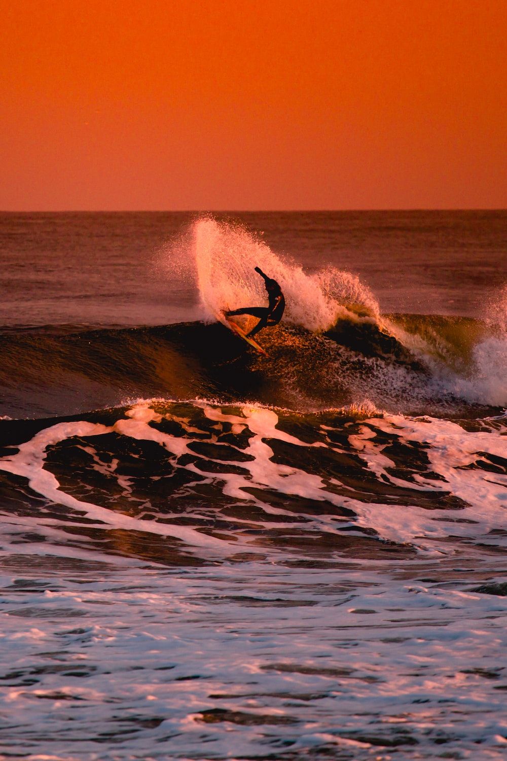 A surfer rides a wave during a sunset - Surf