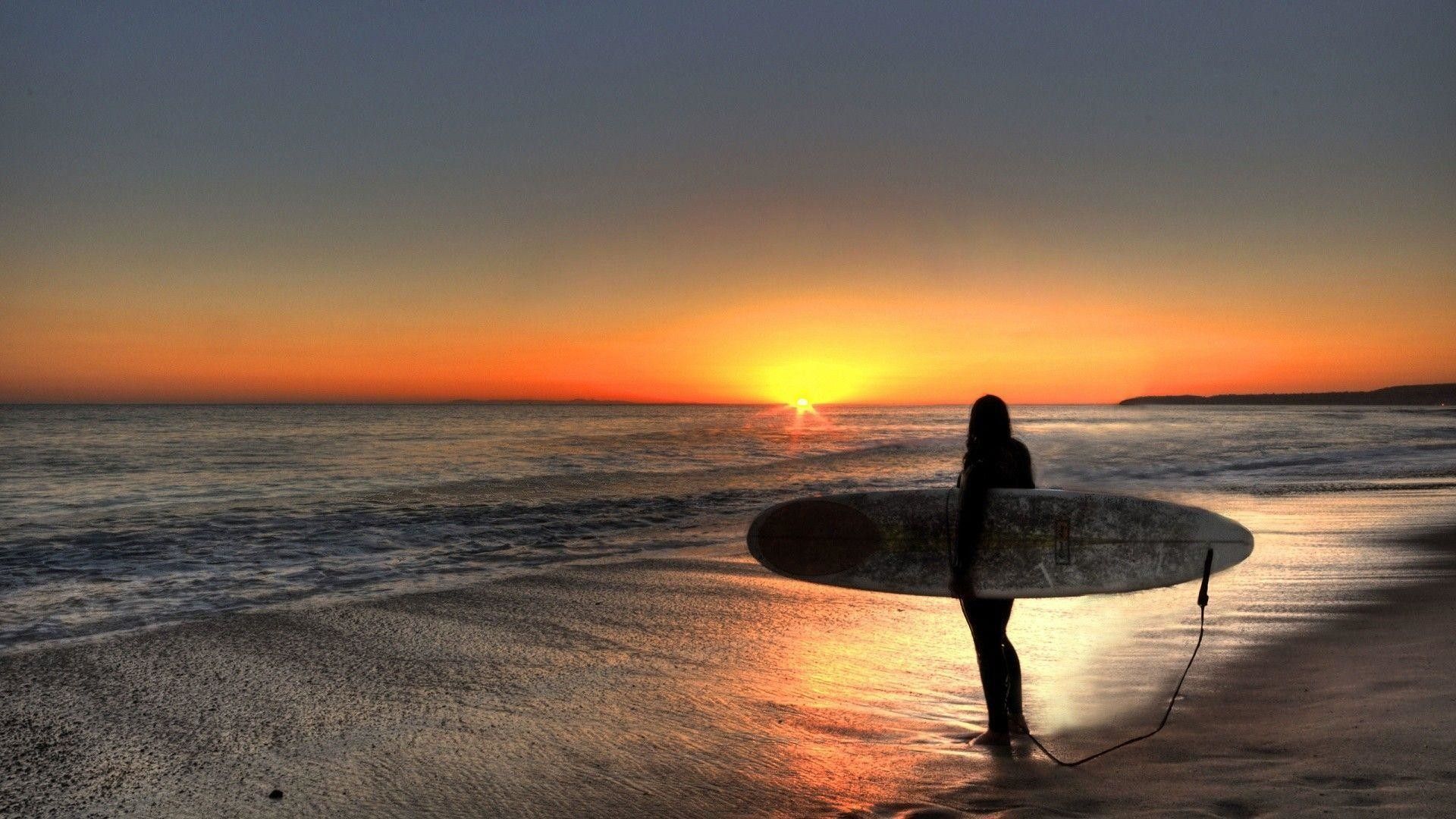 A surfer standing on the beach at sunset - Surf