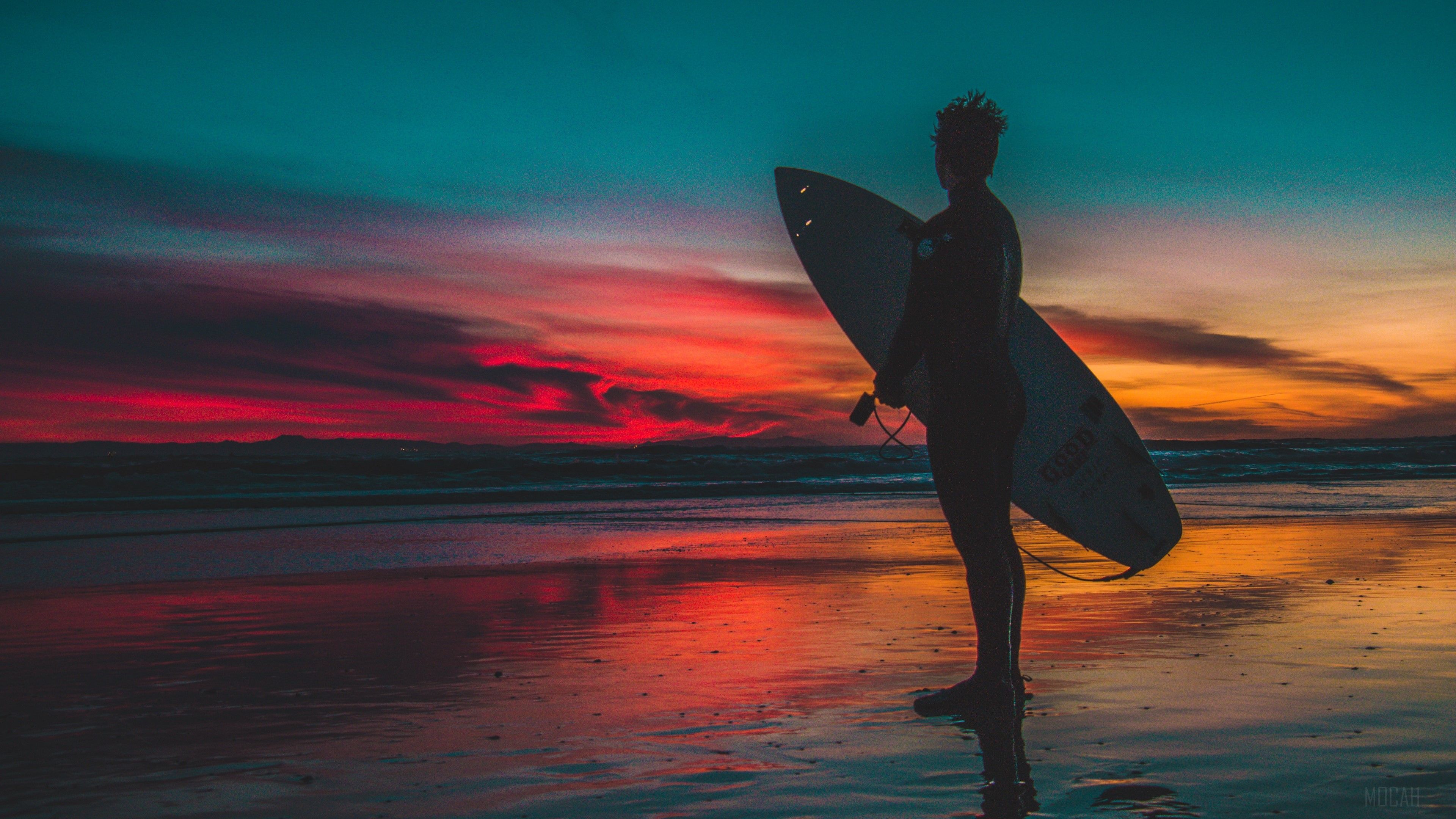 A man standing on the beach holding his surfboard - Surf