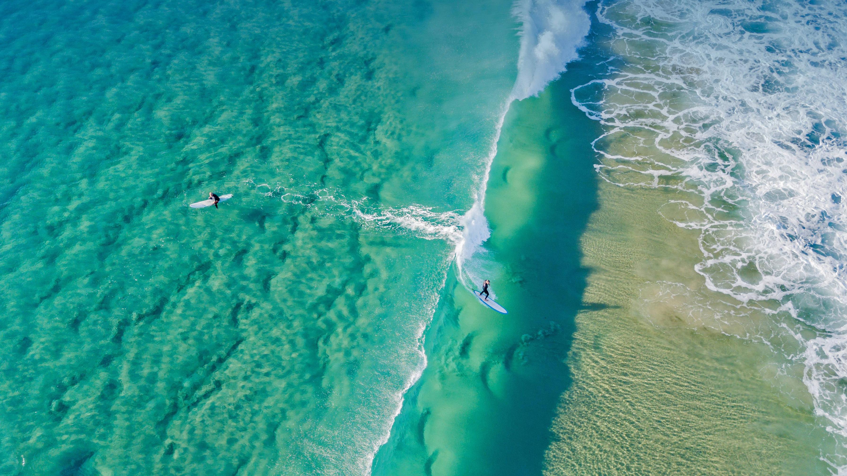 Aerial view of two surfers paddling out into the ocean. - Surf