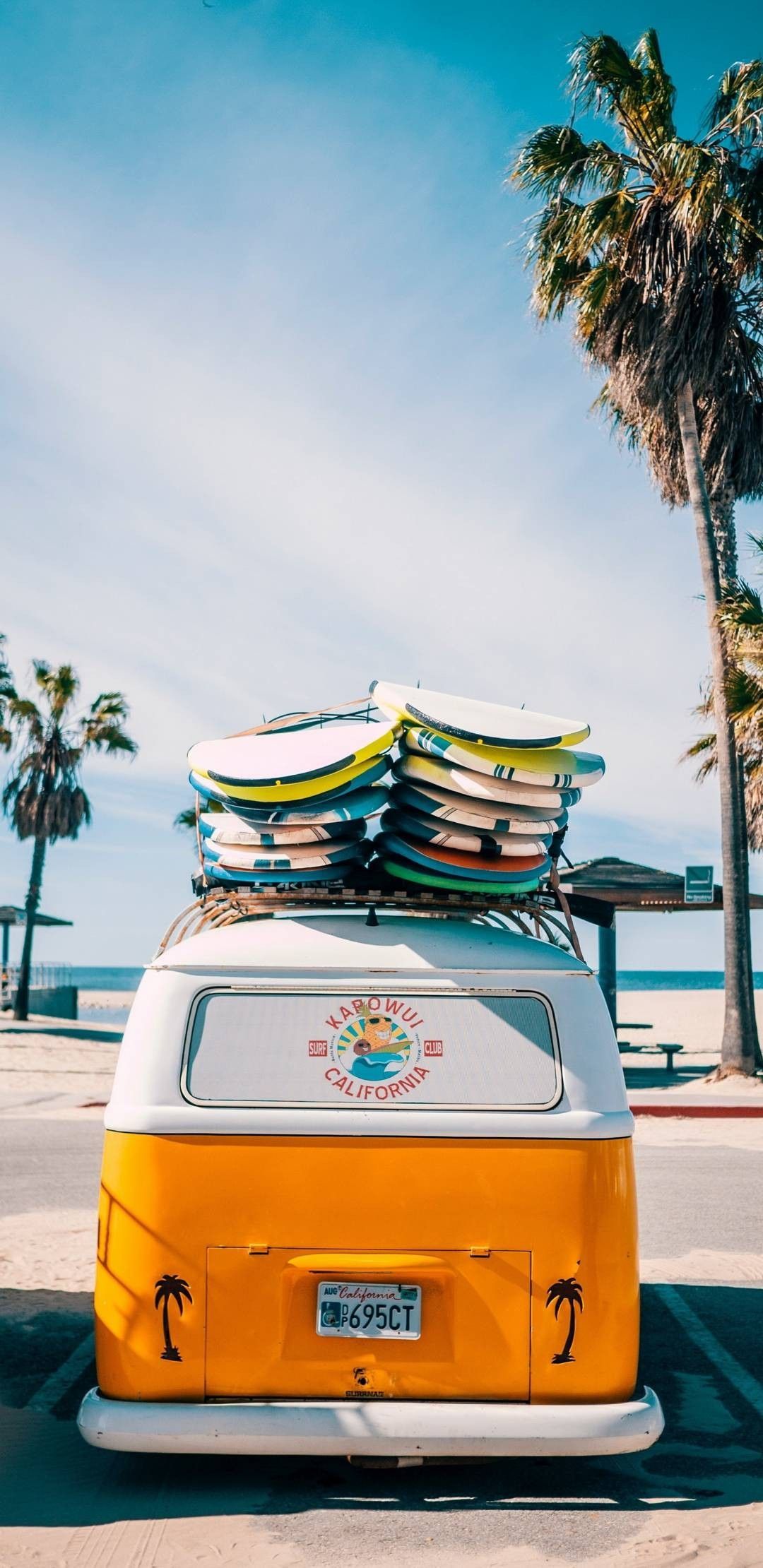 Surfboards on top of a yellow and white van parked on the beach - Surf