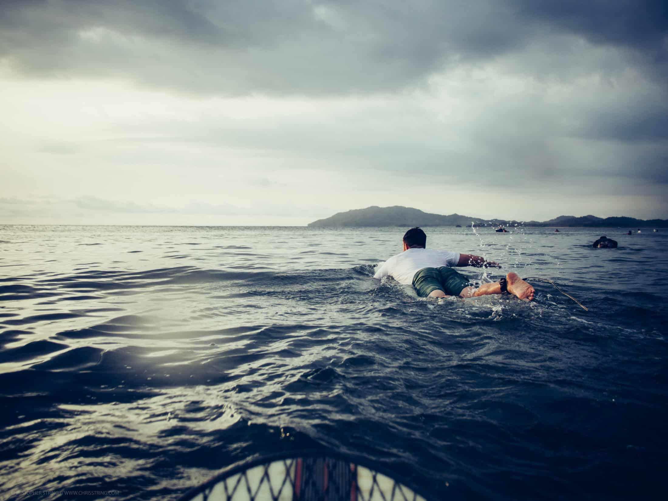 A surfer paddles out to sea in the distance - Surf