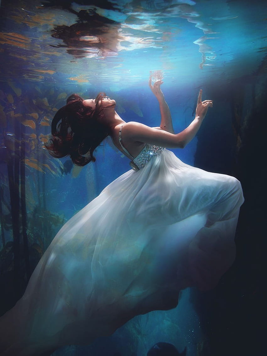 A woman in a white dress is underwater, surrounded by fish. - Underwater