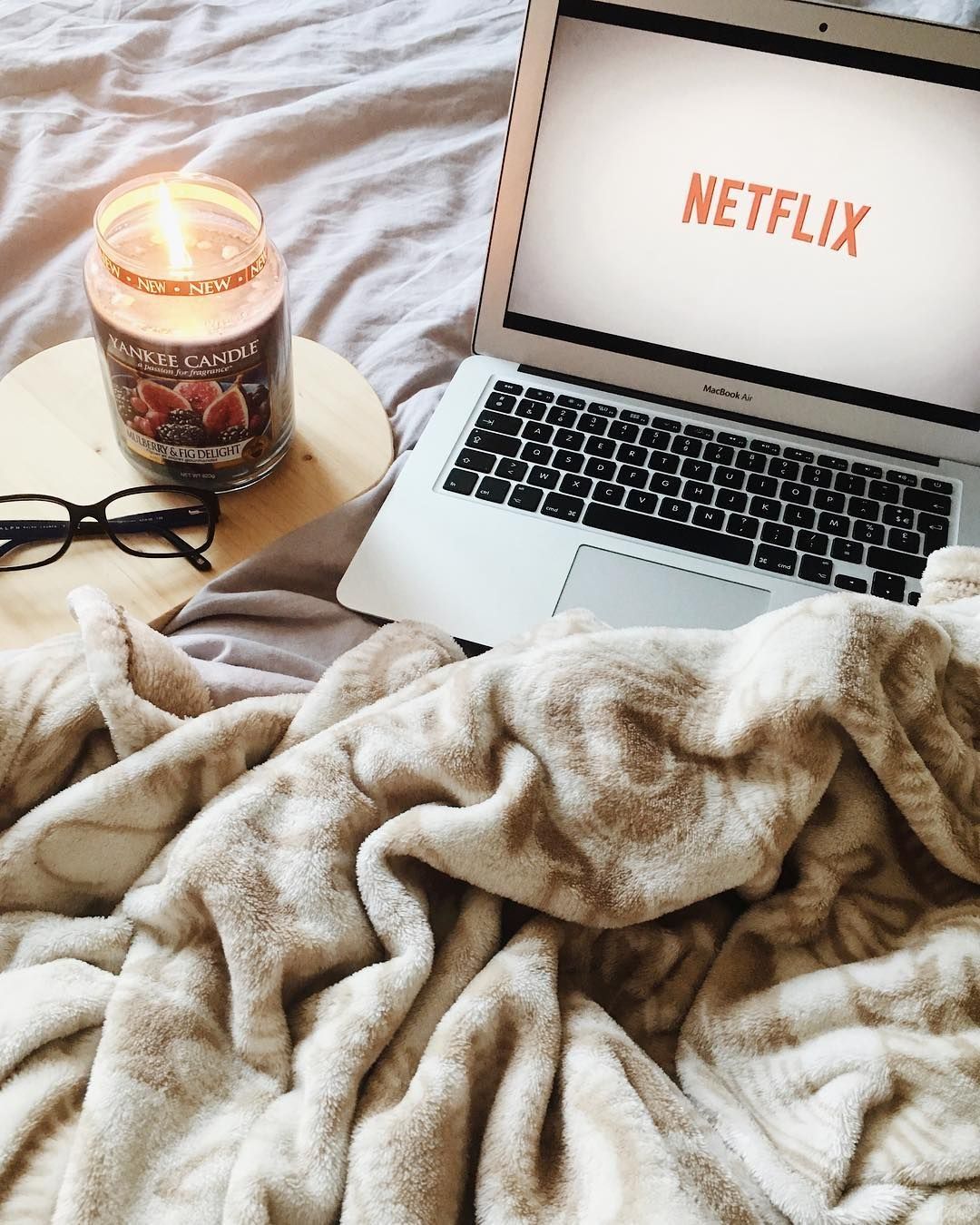 A laptop sitting on top of bed with candle - Netflix