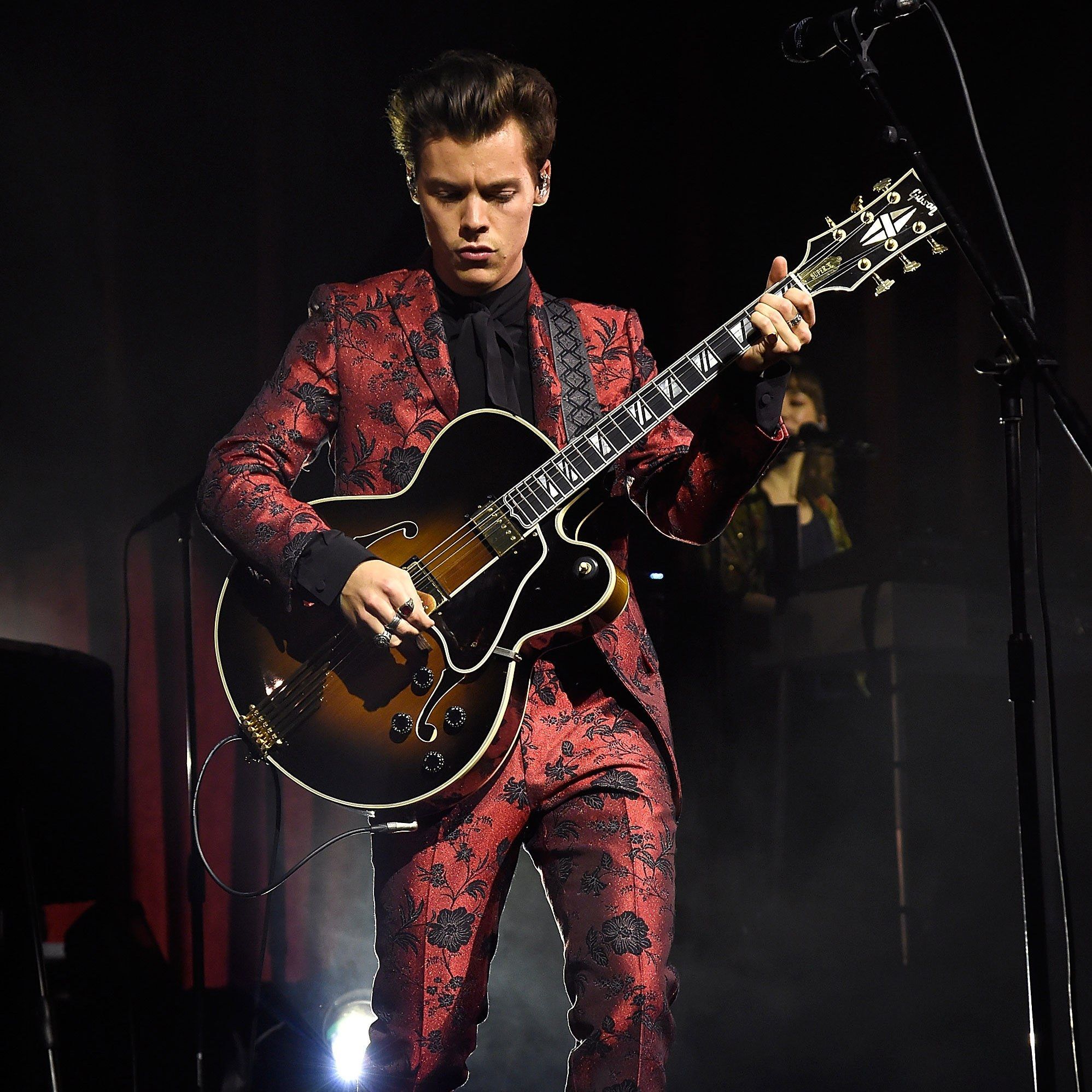 A man in red suit playing guitar on stage - Harry Styles