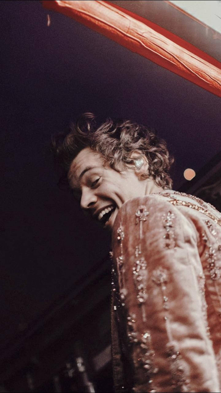 A man is laughing while holding his phone - Harry Styles