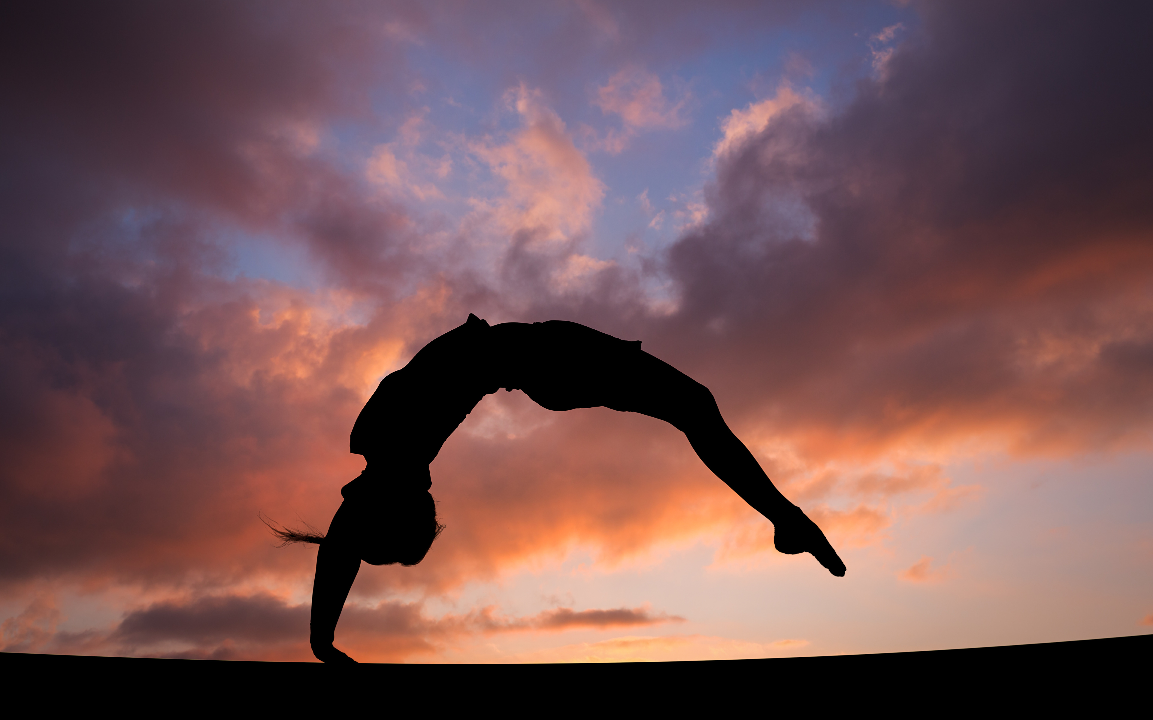 A woman does a back bend with a sunset in the background. - Gymnastics