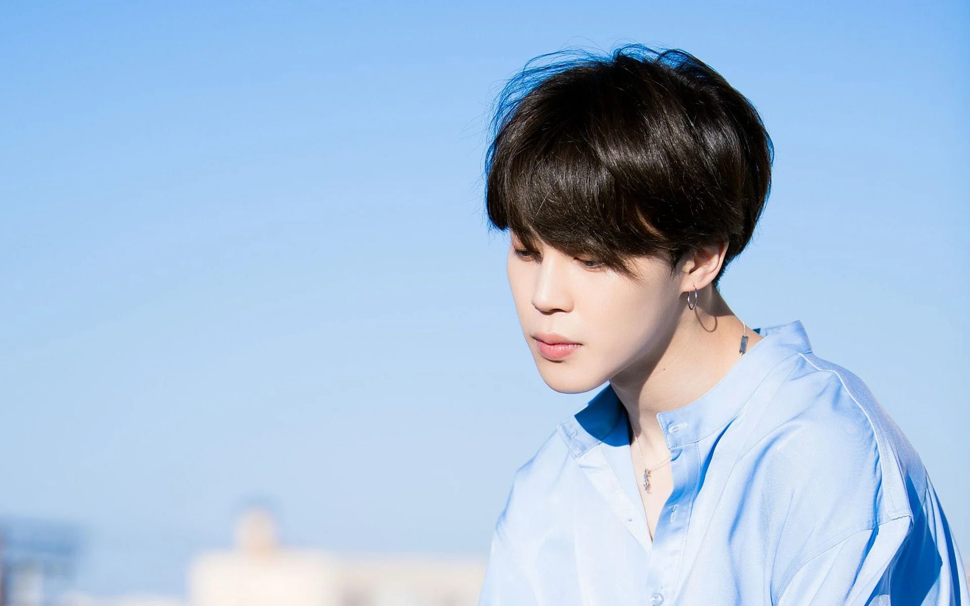 BTS member Jin looking down with a blue sky in the background - Jimin