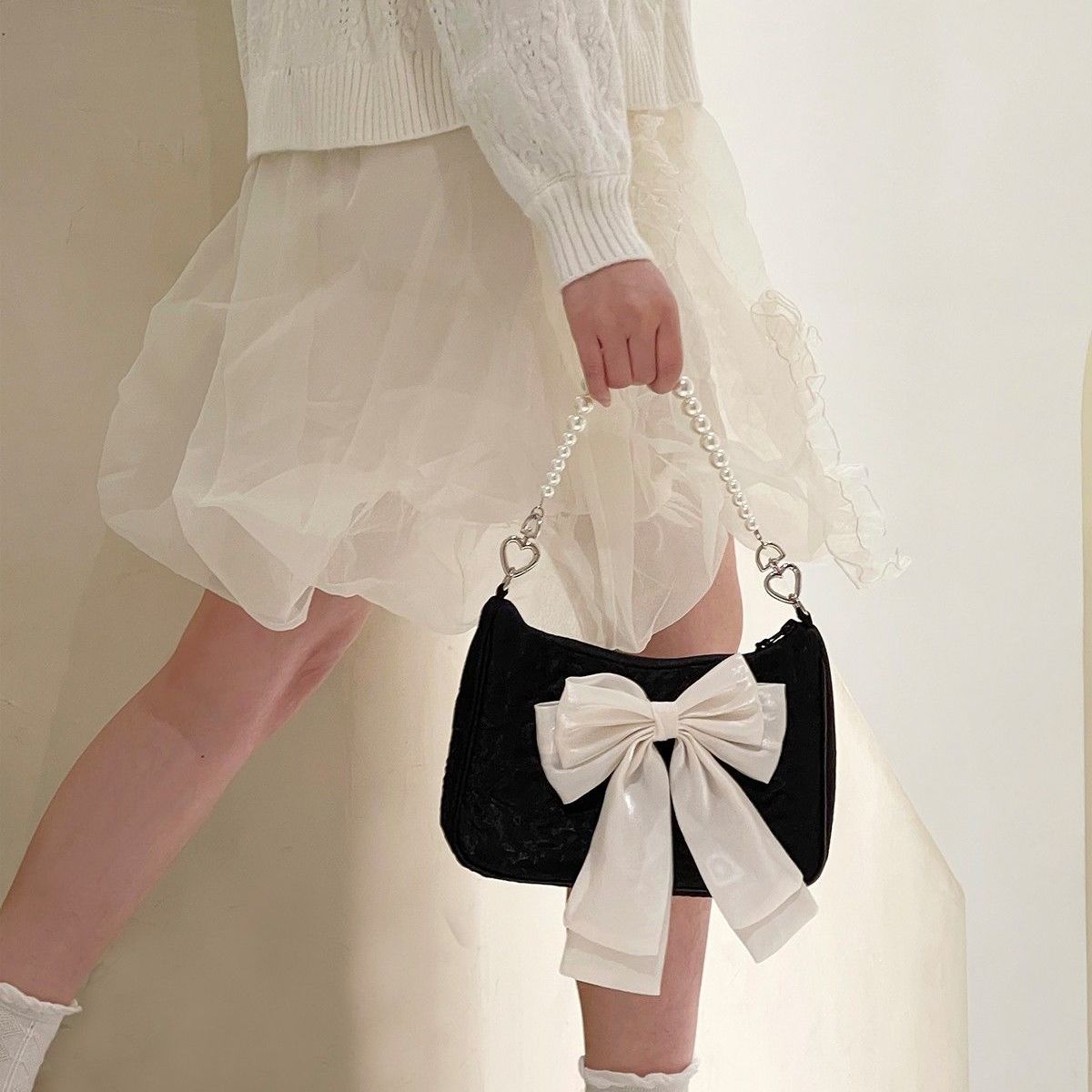 A woman in a white dress holding a black bag with a white bow. - Coquette