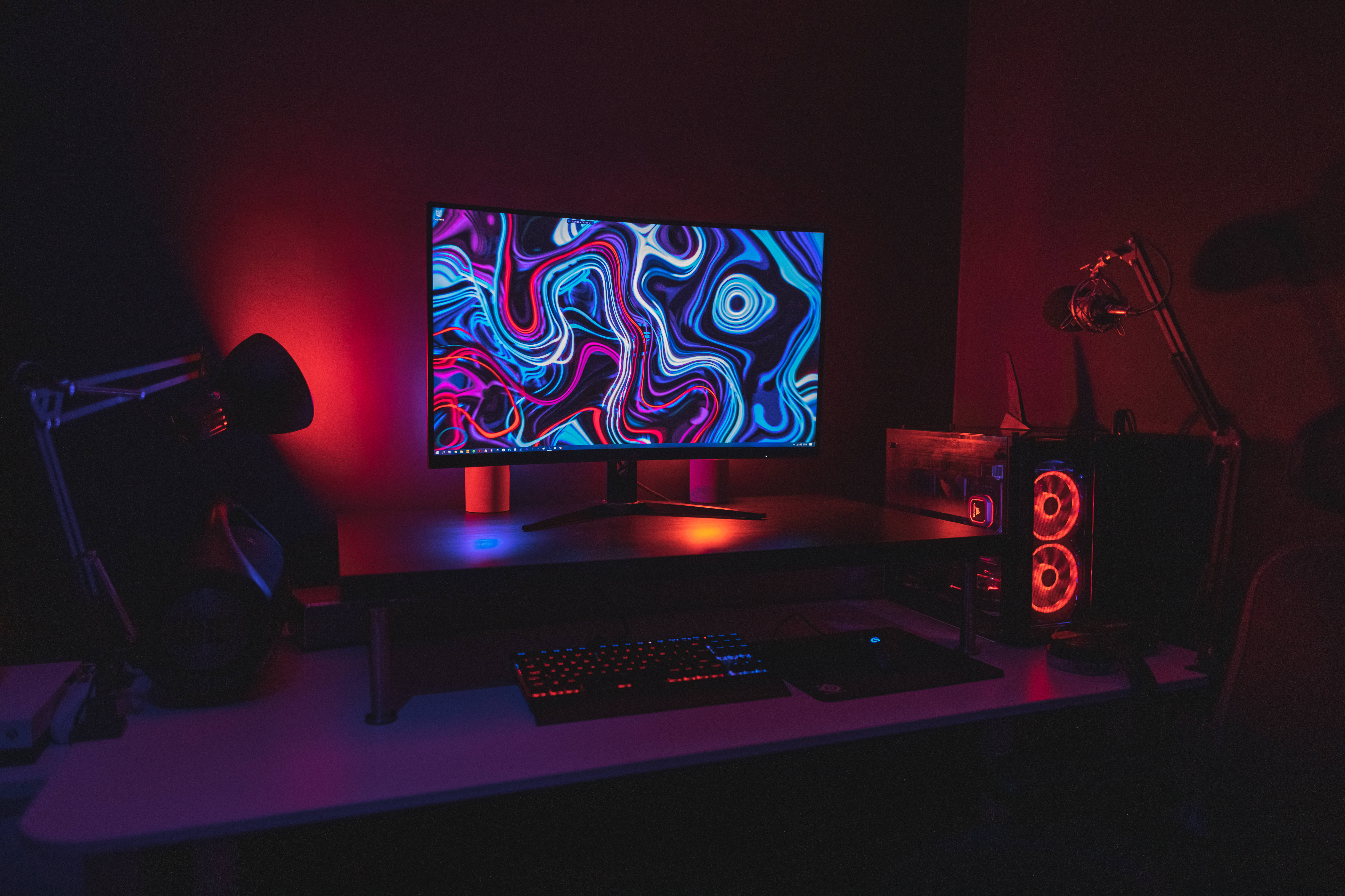 A desk with a computer and monitor lit up by red and blue lights - Gaming
