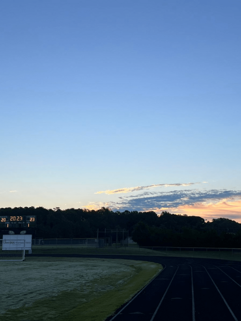 A sports field with a scoreboard and running track at sunset. - School