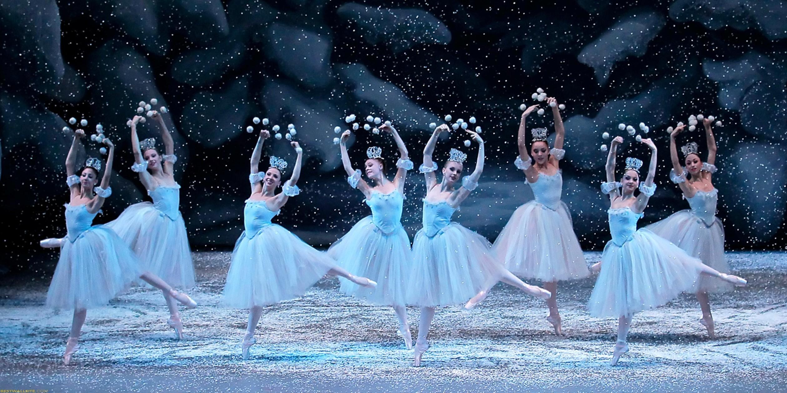 Ballerinas in blue and white tutus stand in a line with arms raised, creating a snowflake effect with their hands. - Ballet