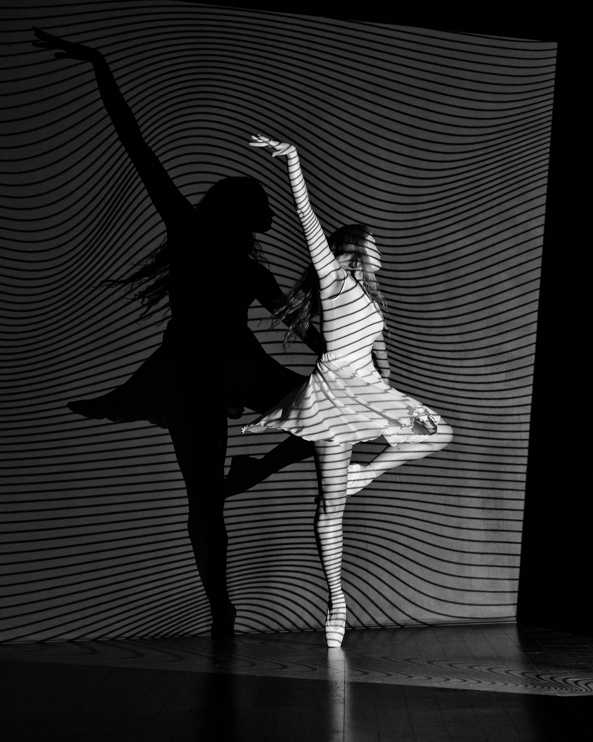 A woman dances in front of a wall with a light painting of a woman dancing behind her. - Ballet