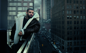 Drake standing on a balcony with a city in the background - Drake