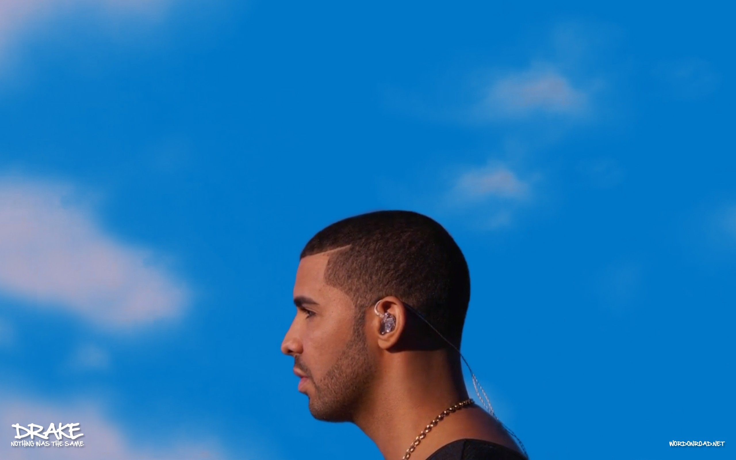 A picture of Drake looking off into the distance with a blue sky in the background. - Drake