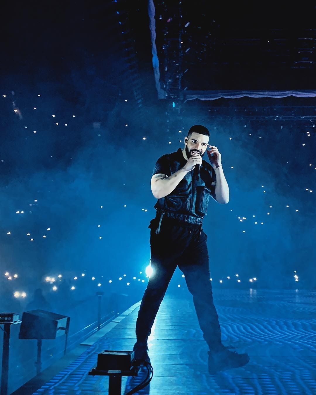 Drake on stage singing in a dark room with blue lights - Drake