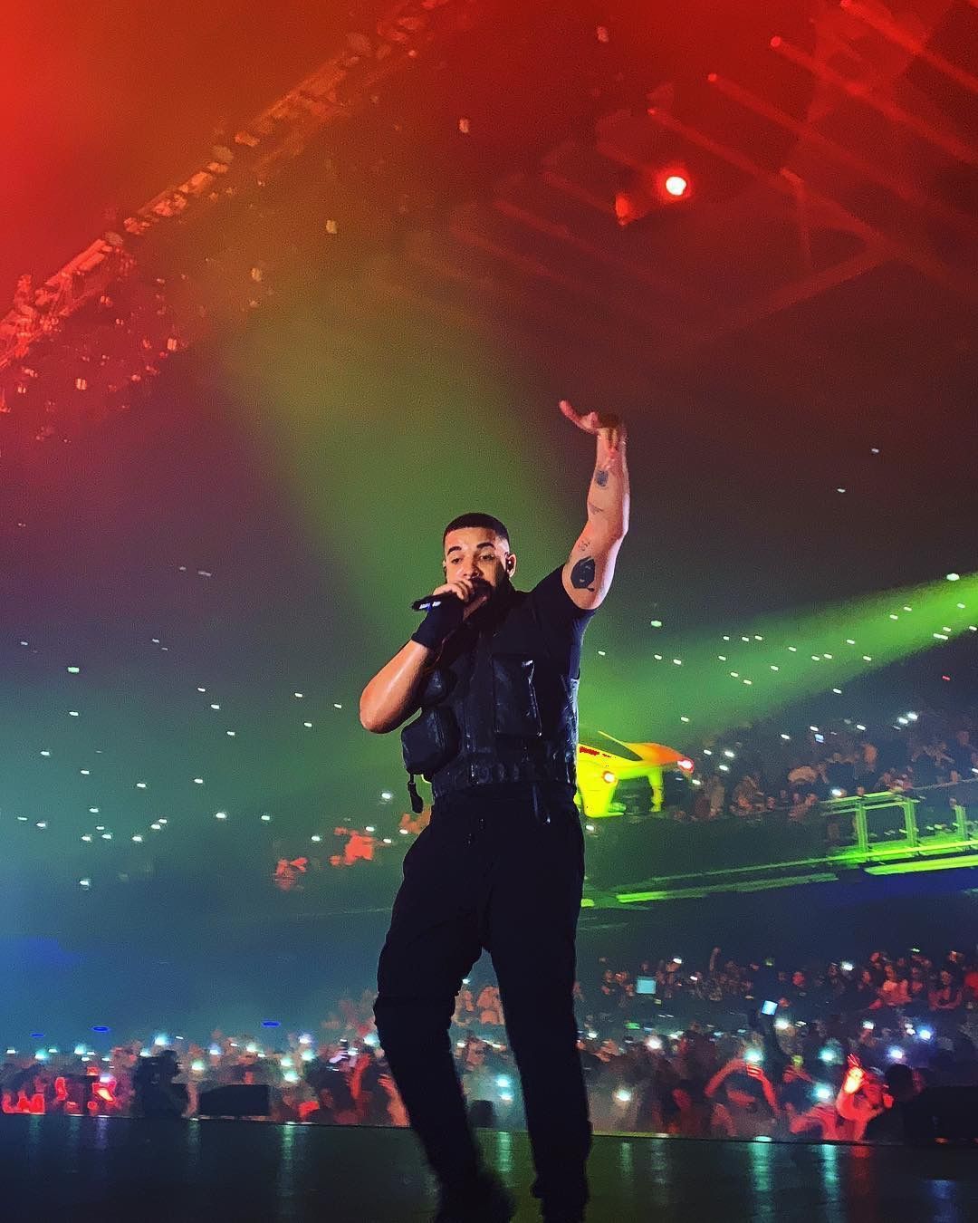 Drake on stage in a black vest and jeans holding a microphone - Drake