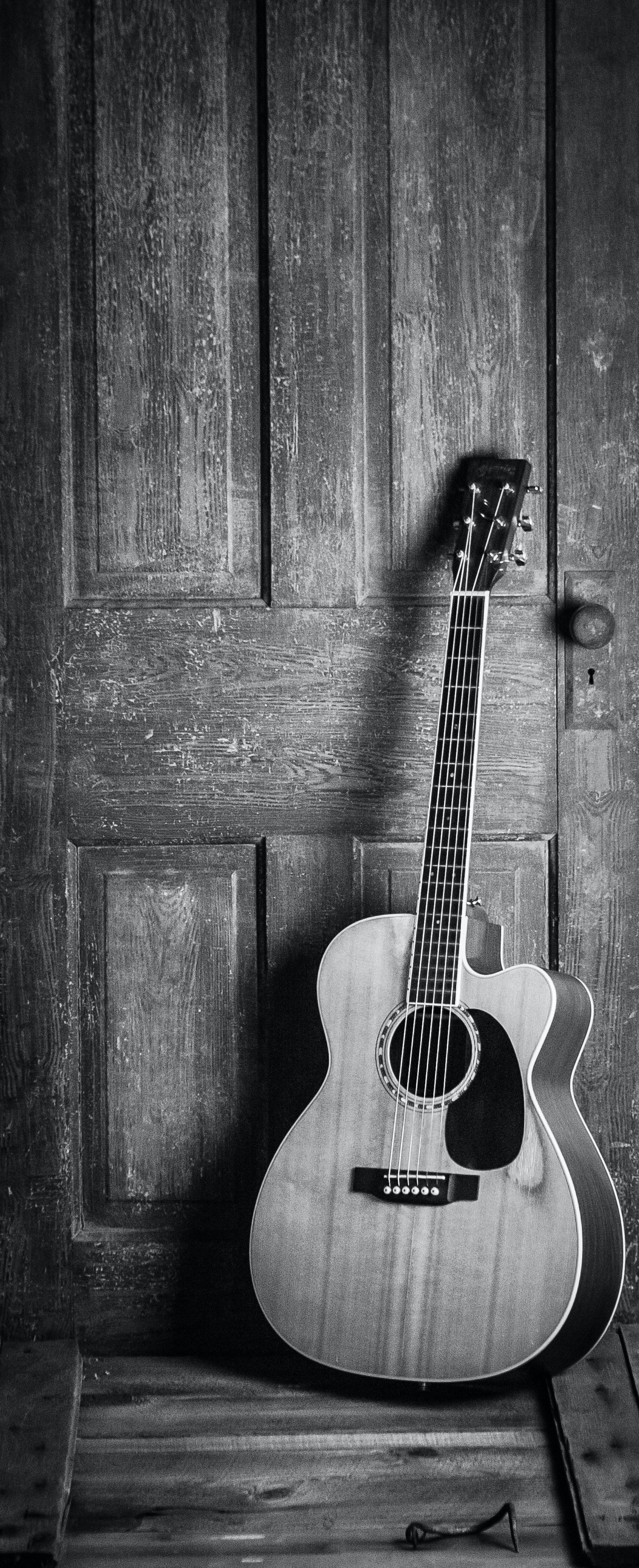 Black and white photo of a guitar leaning against a wooden door. - Guitar
