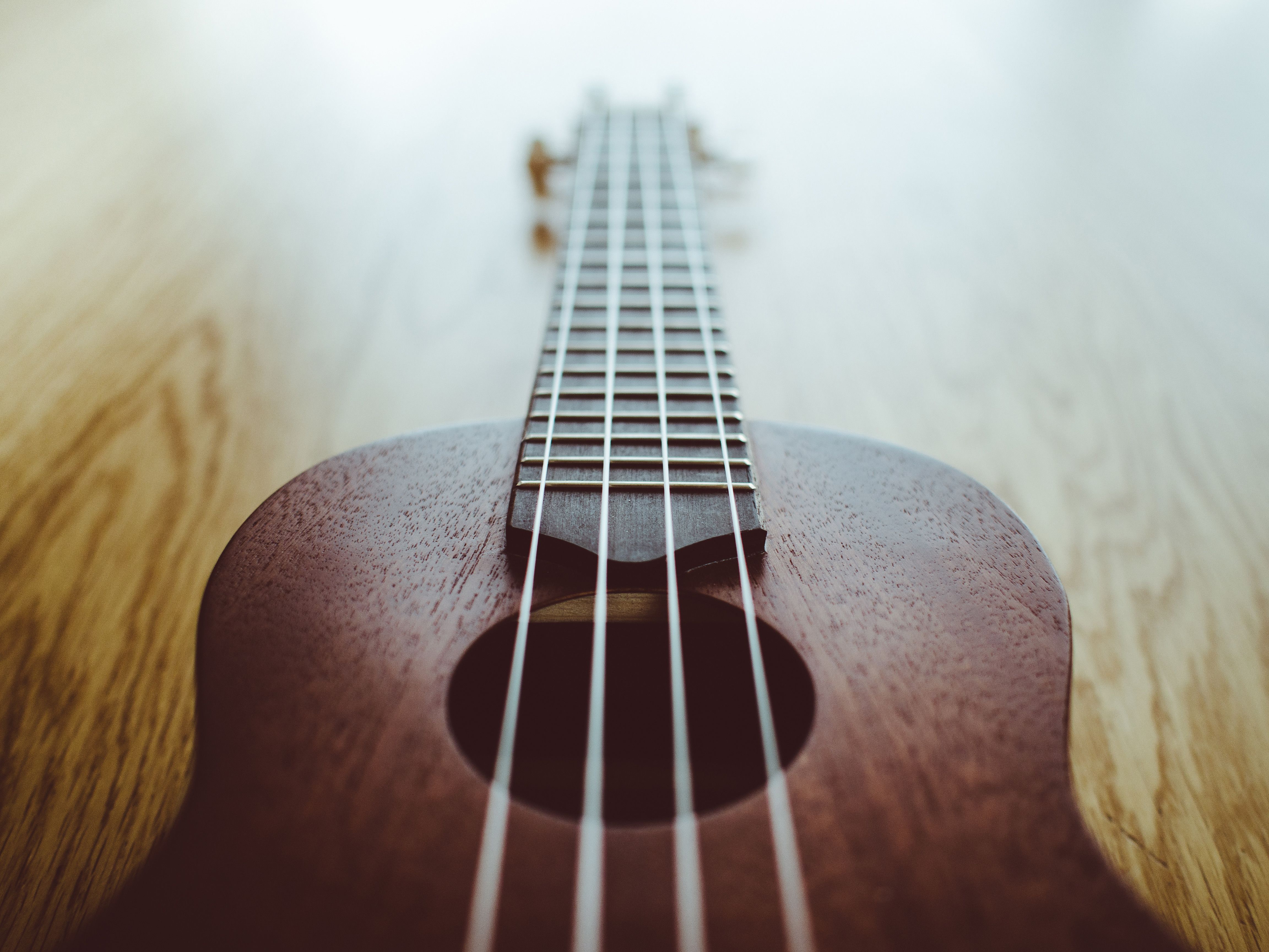 A brown ukulele sits on a wooden table. - Guitar