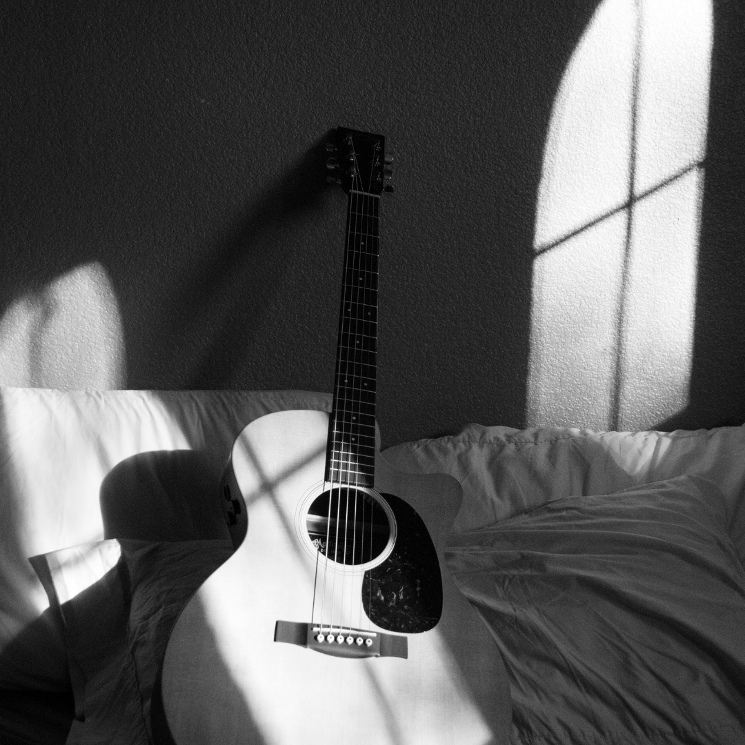 A guitar sitting on the bed next to pillows - Guitar