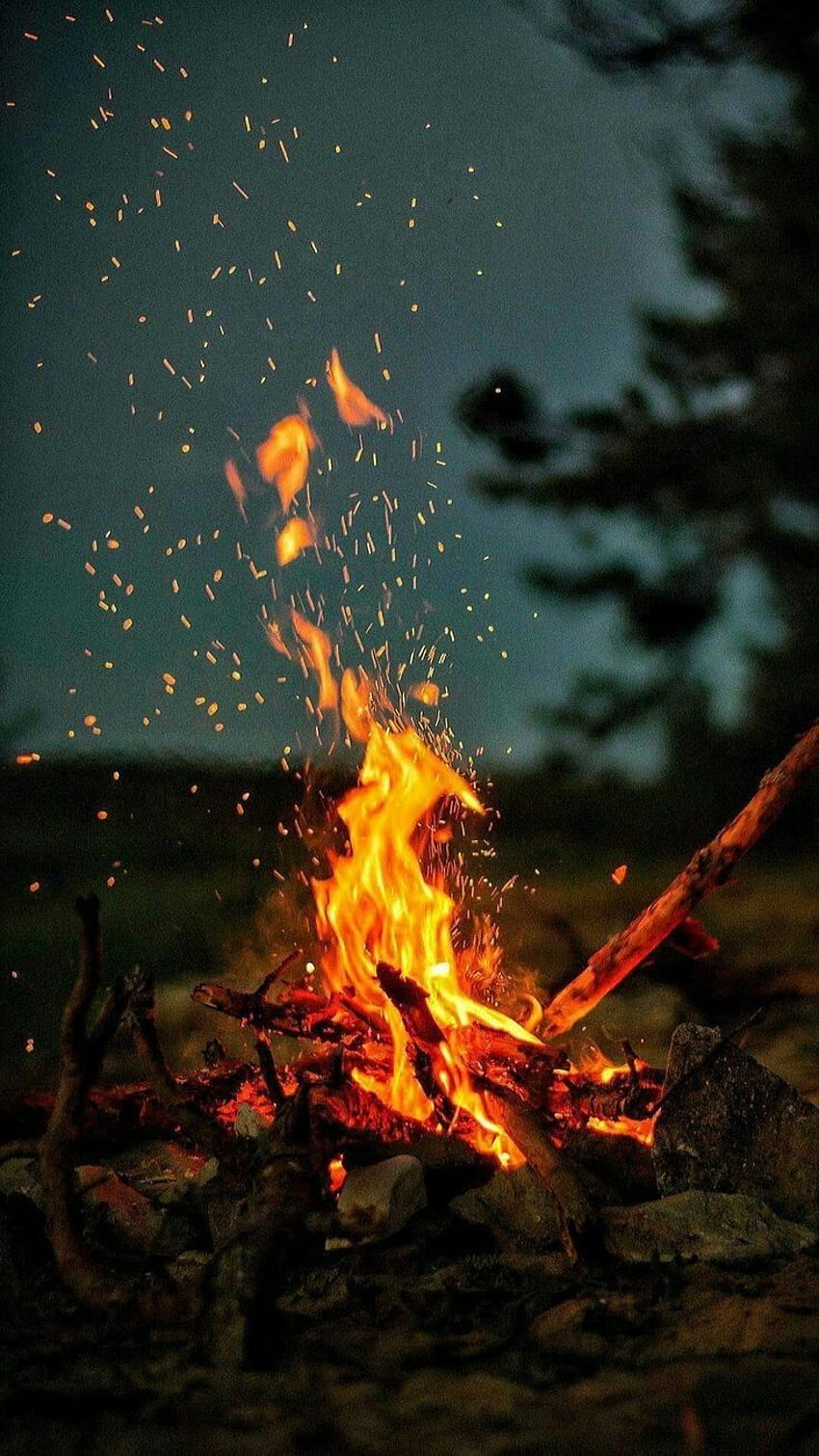 A campfire burns in the dark, sparks flying in all directions. - Cozy, western, fire